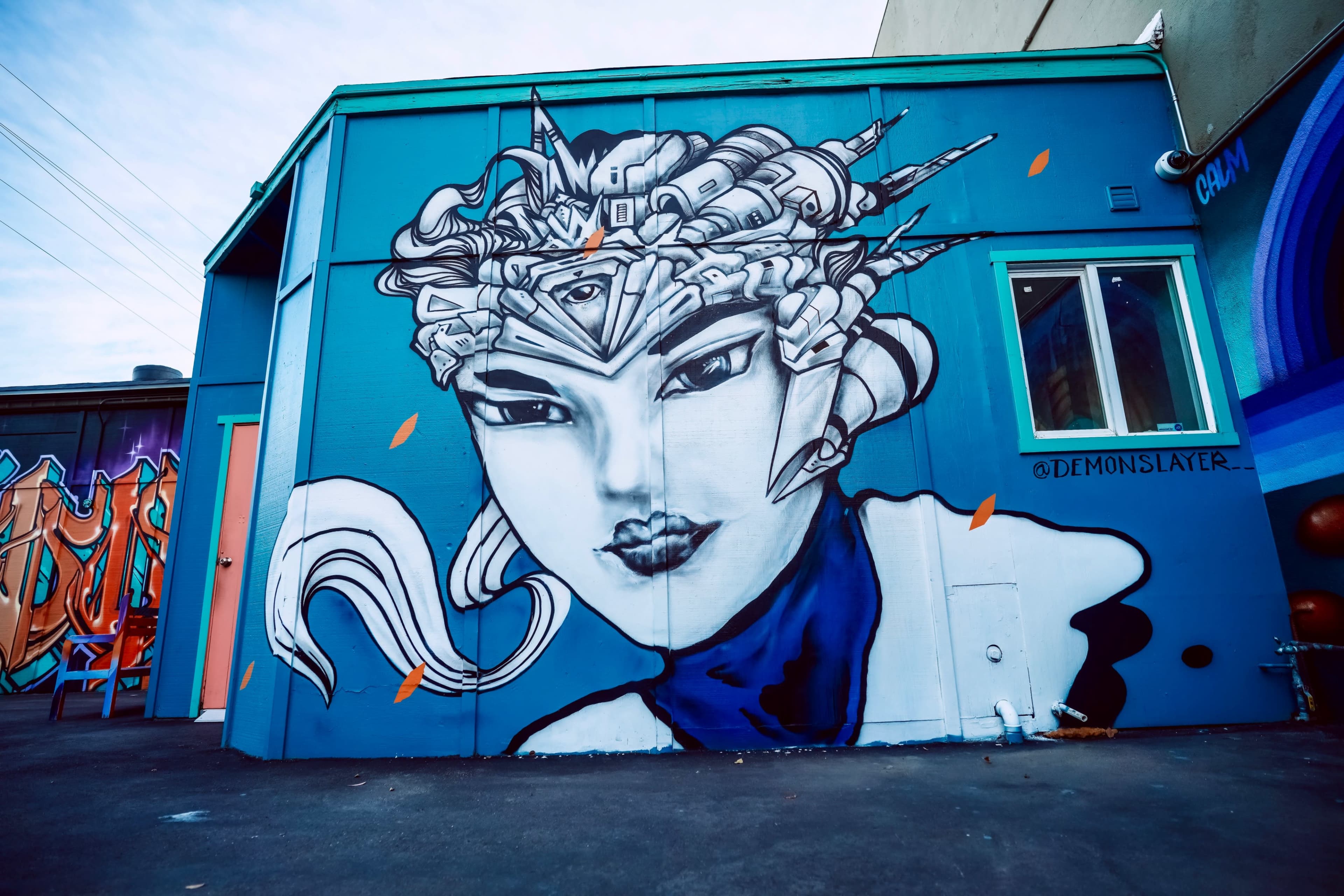 A large mural of a woman with intricate, mechanical hair is painted on the side of a blue building.