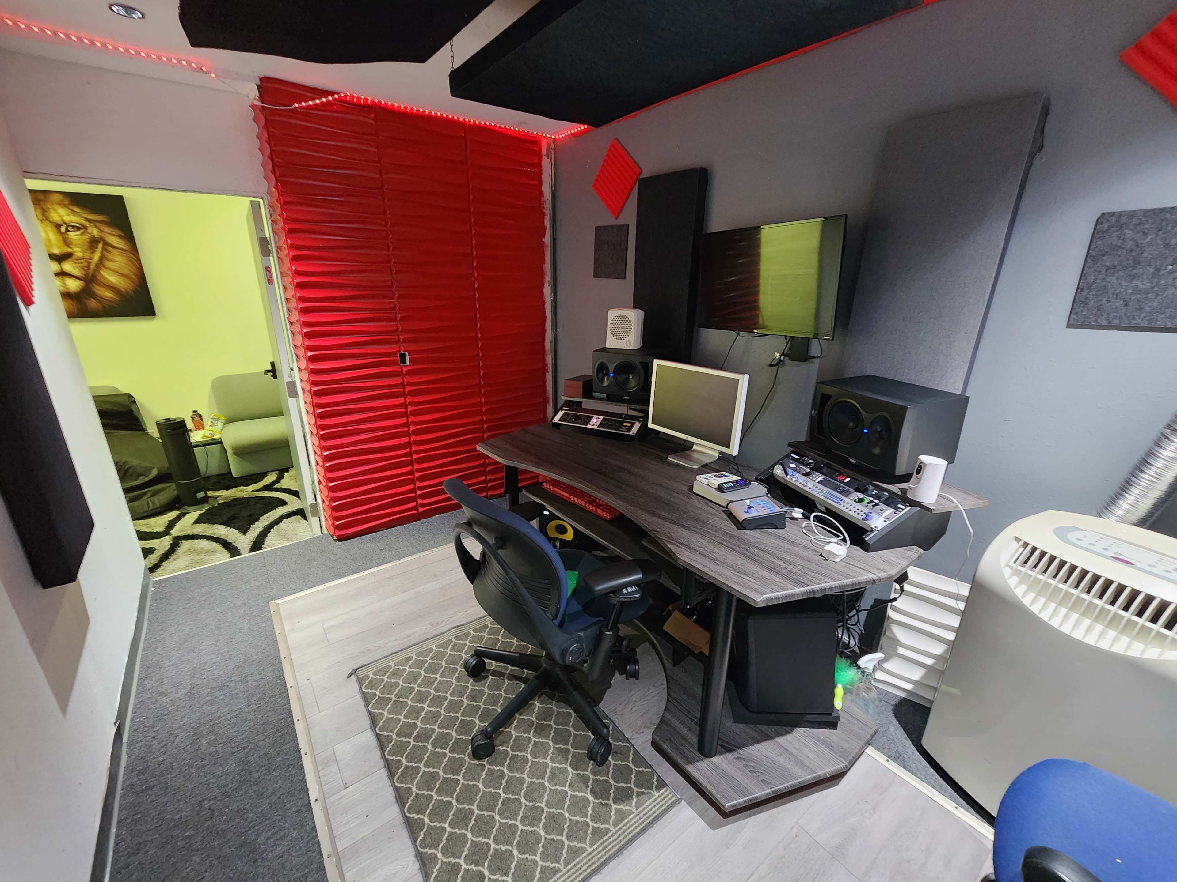 A compact recording studio features a desk with audio equipment, surrounded by soundproofing panels and red accent walls.