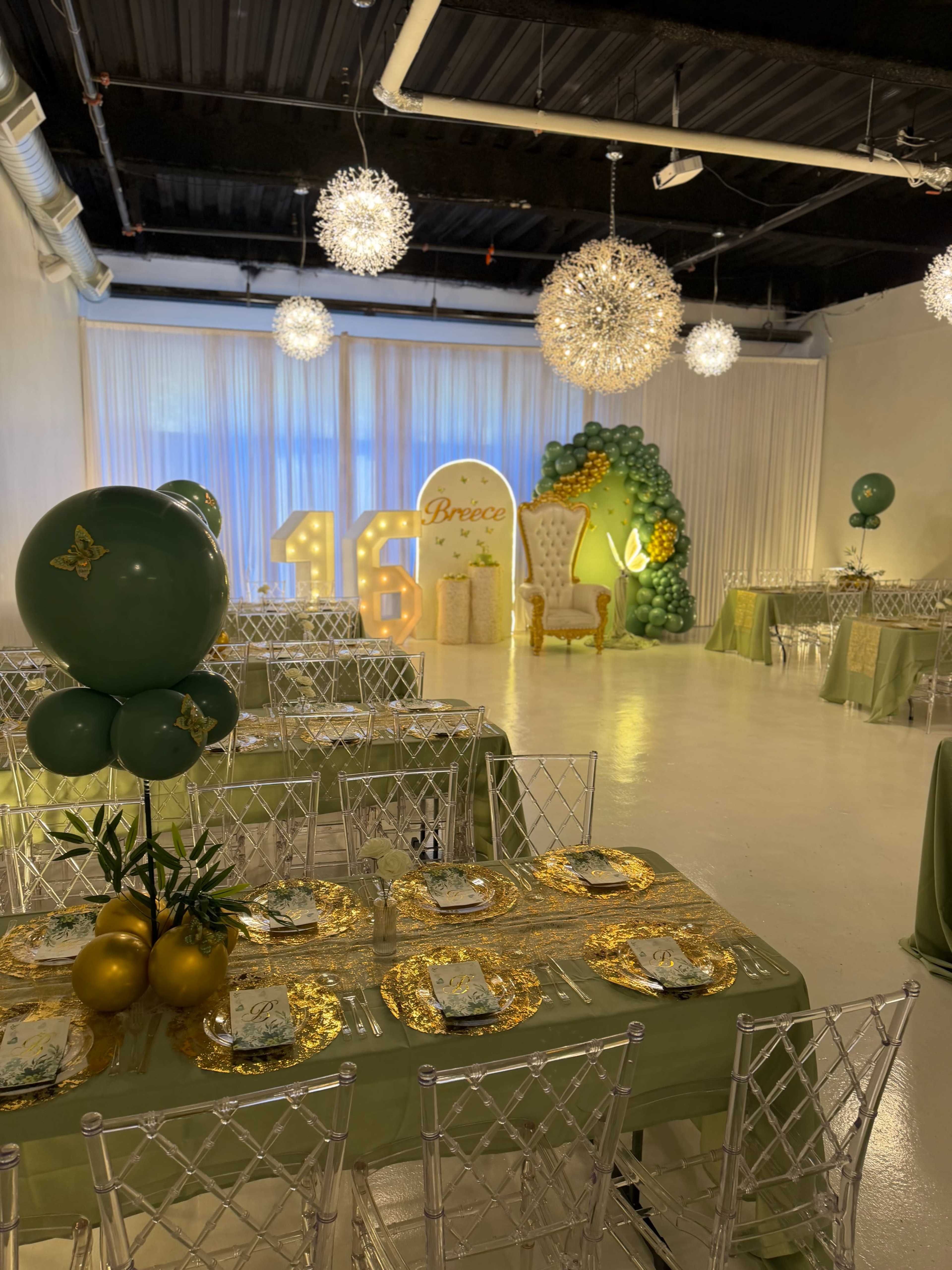 The image shows a decorated event space featuring green and gold-themed tables with elegant seating, a backdrop of balloons, and illuminated number displays for a 16th birthday celebration.
