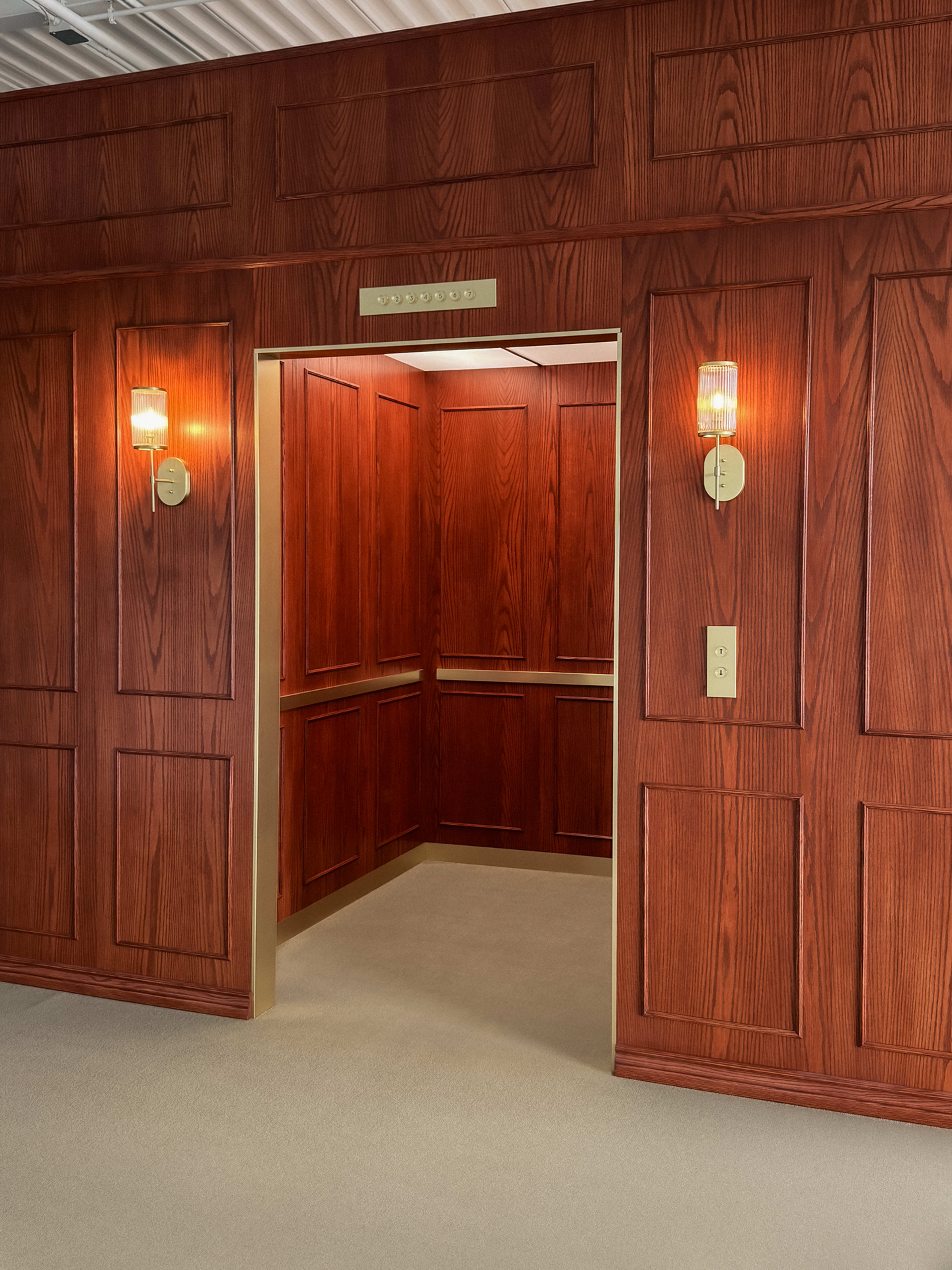 The image shows an elevator entrance with wooden paneling and warm light fixtures.