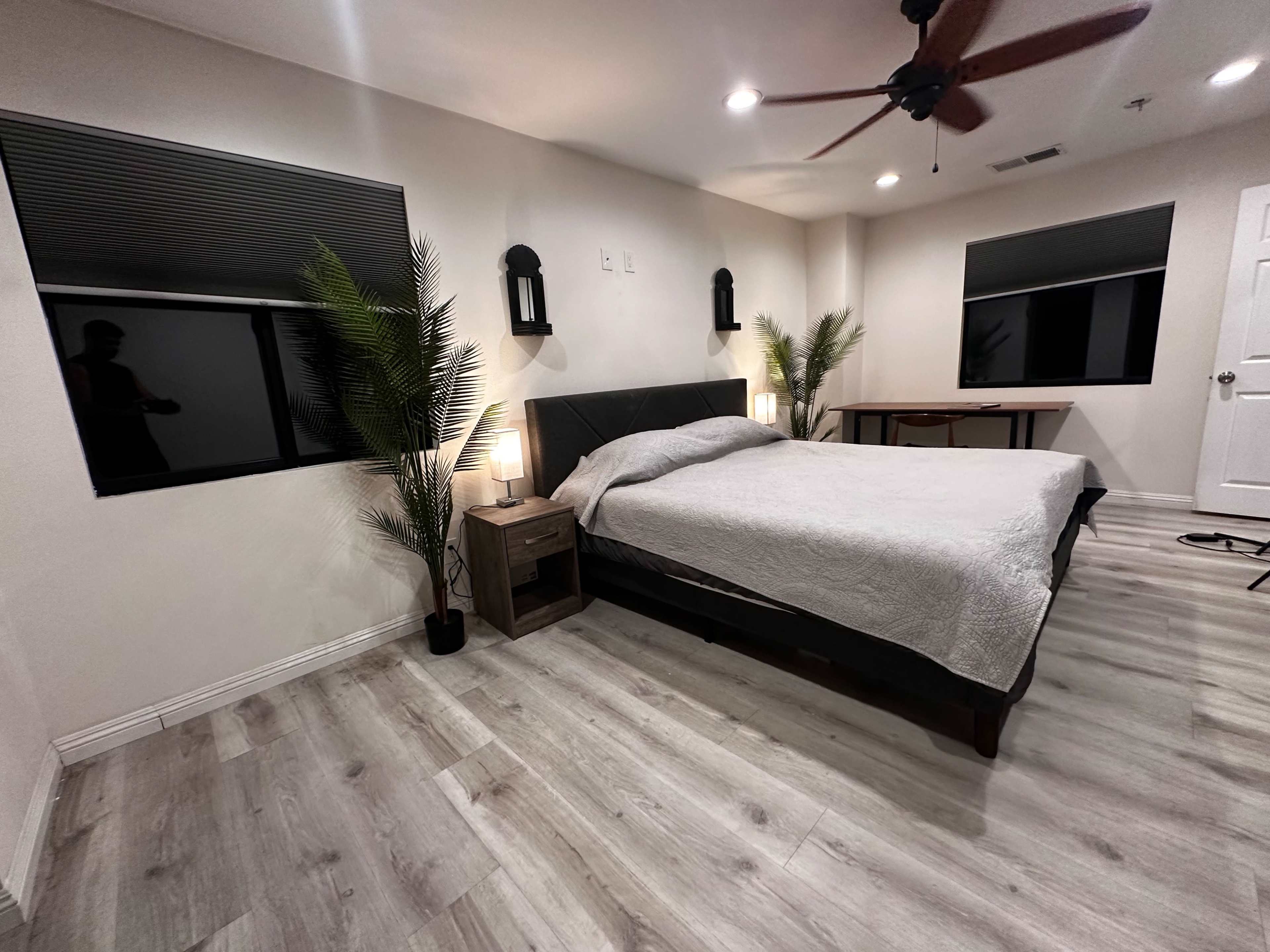 A modern bedroom with a king-sized bed, two bedside lamps, and large windows featuring black blinds.