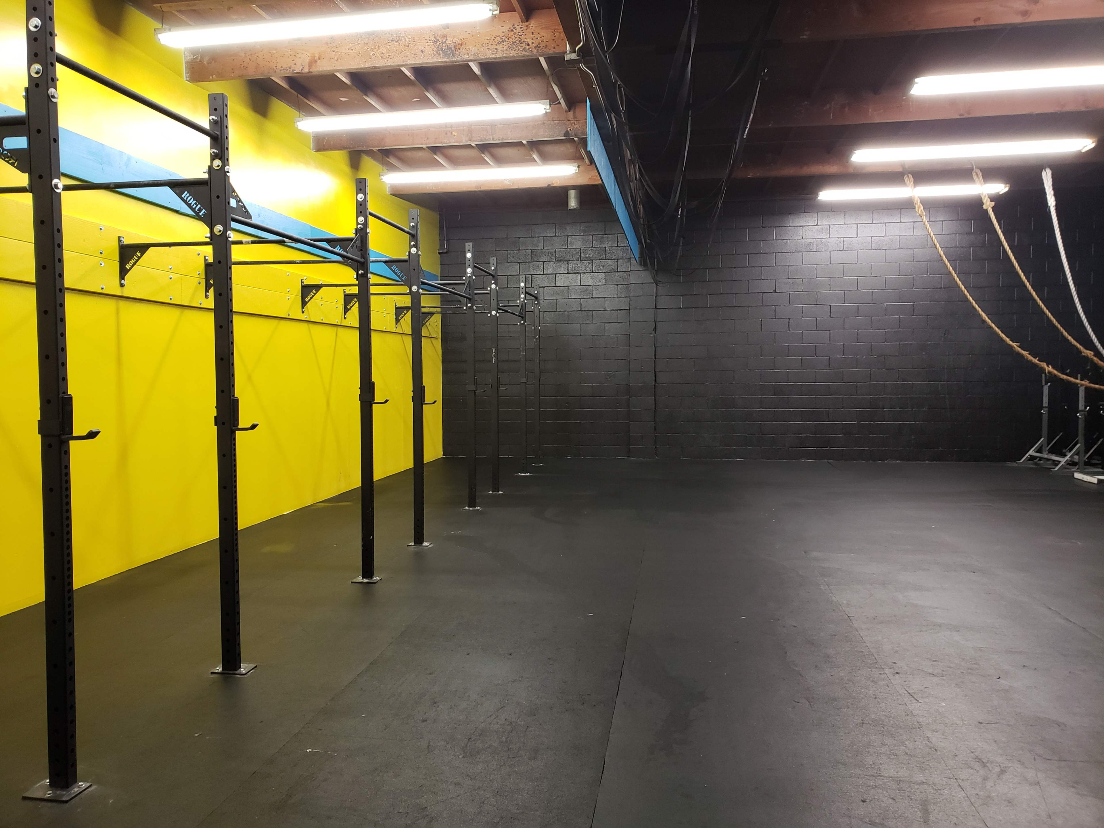 A gym interior with black walls and a bright yellow accent wall, featuring pull-up bars and ropes for exercise.