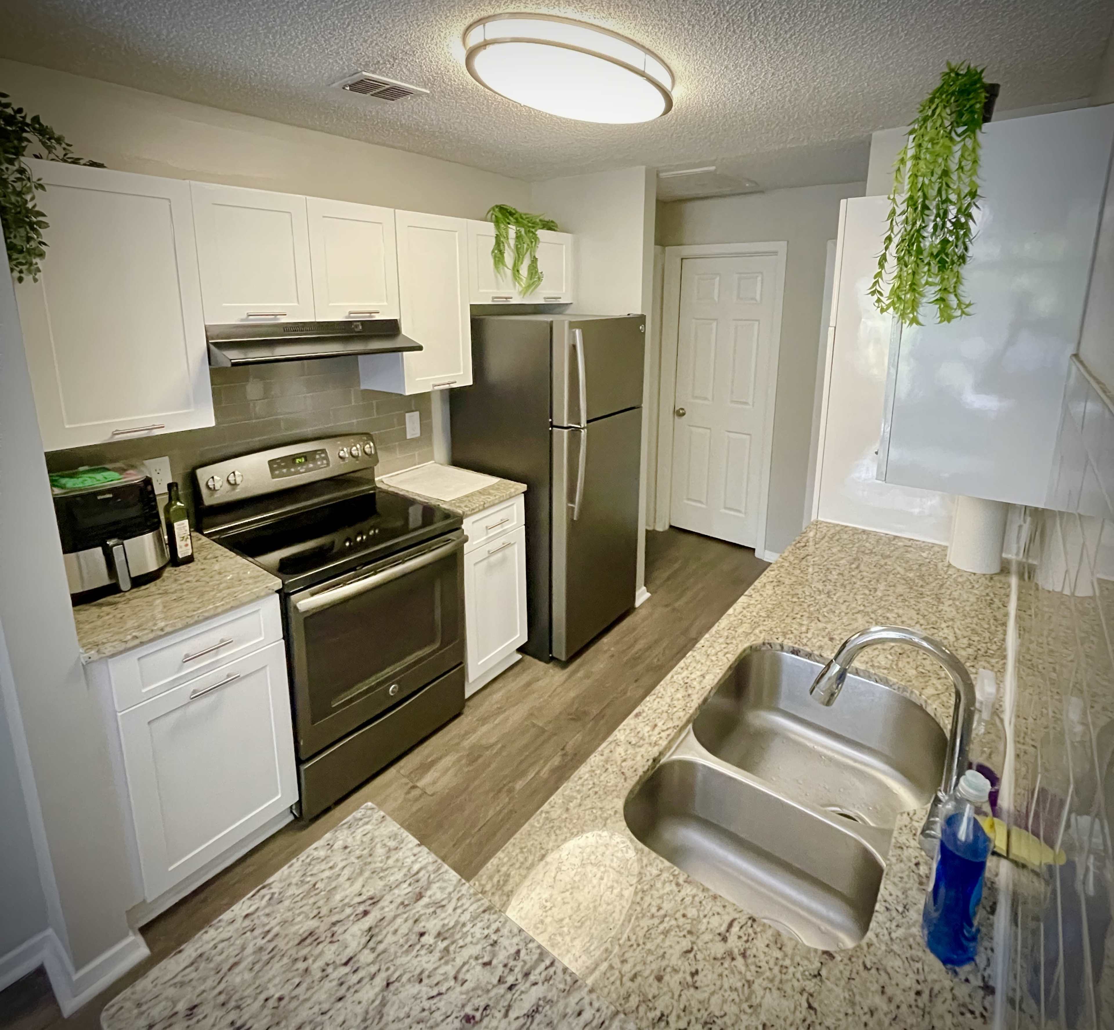 A modern kitchen features white cabinets, a stainless steel refrigerator, and a granite countertop with a double sink.
