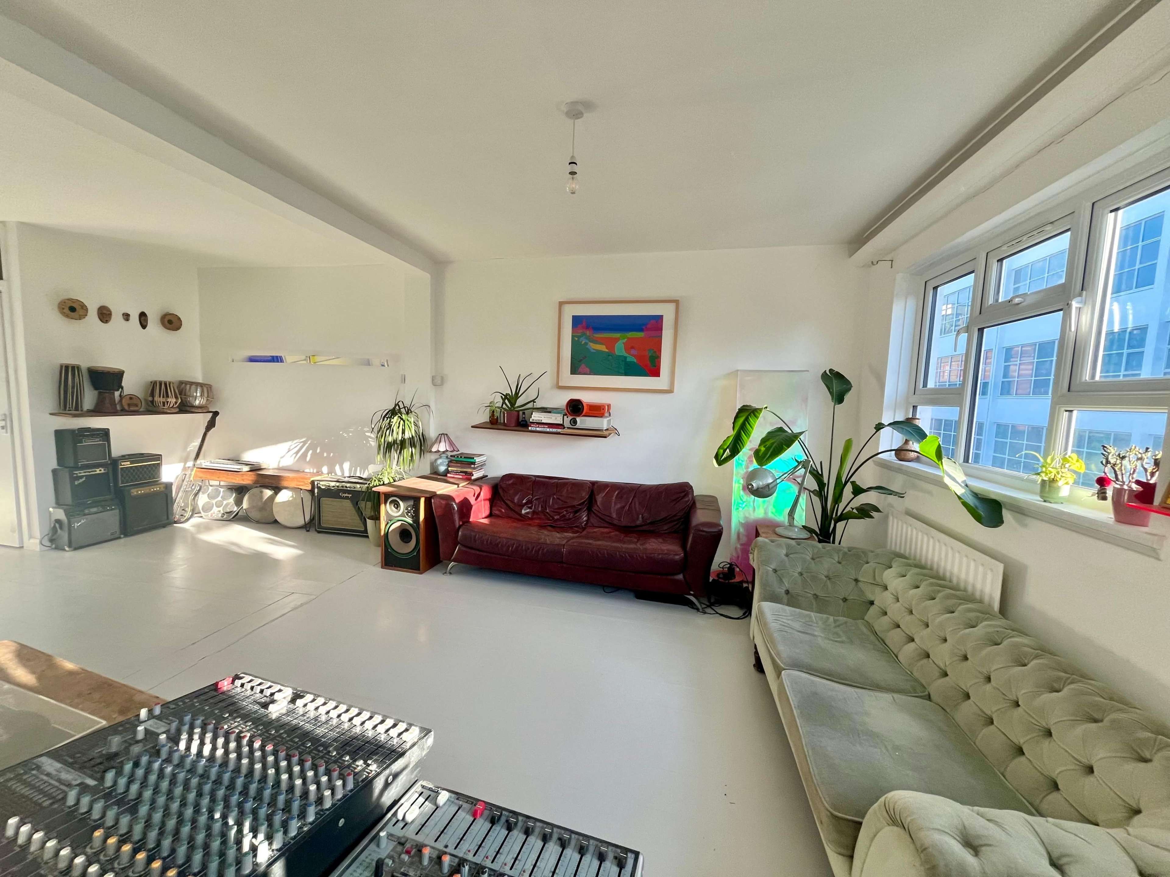 The image shows a spacious, well-lit living room with a mix of modern furniture, including two sofas, a coffee table, and a visible sound mixing board.