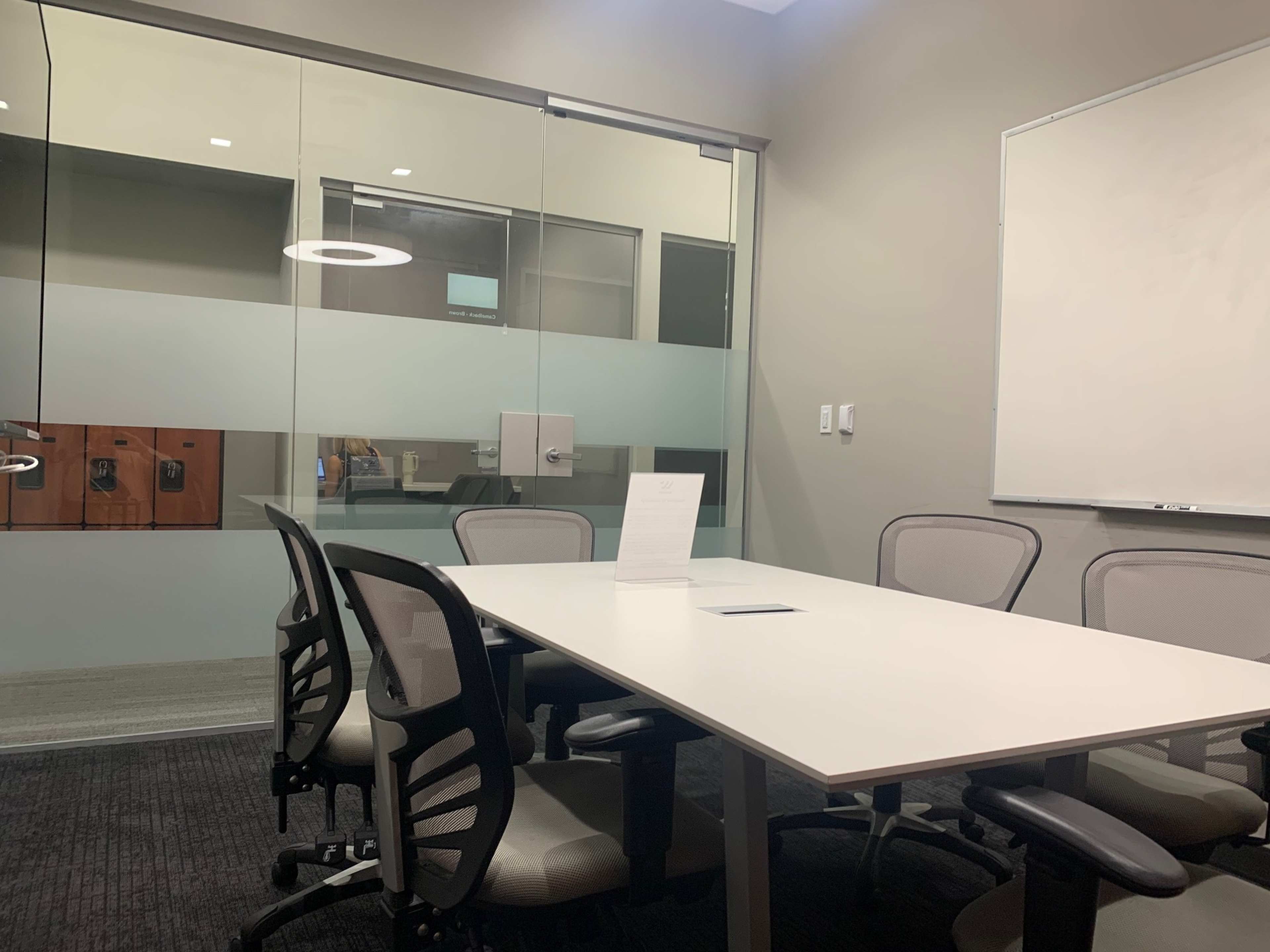 A conference room with a white table, several chairs, a whiteboard, and glass walls.