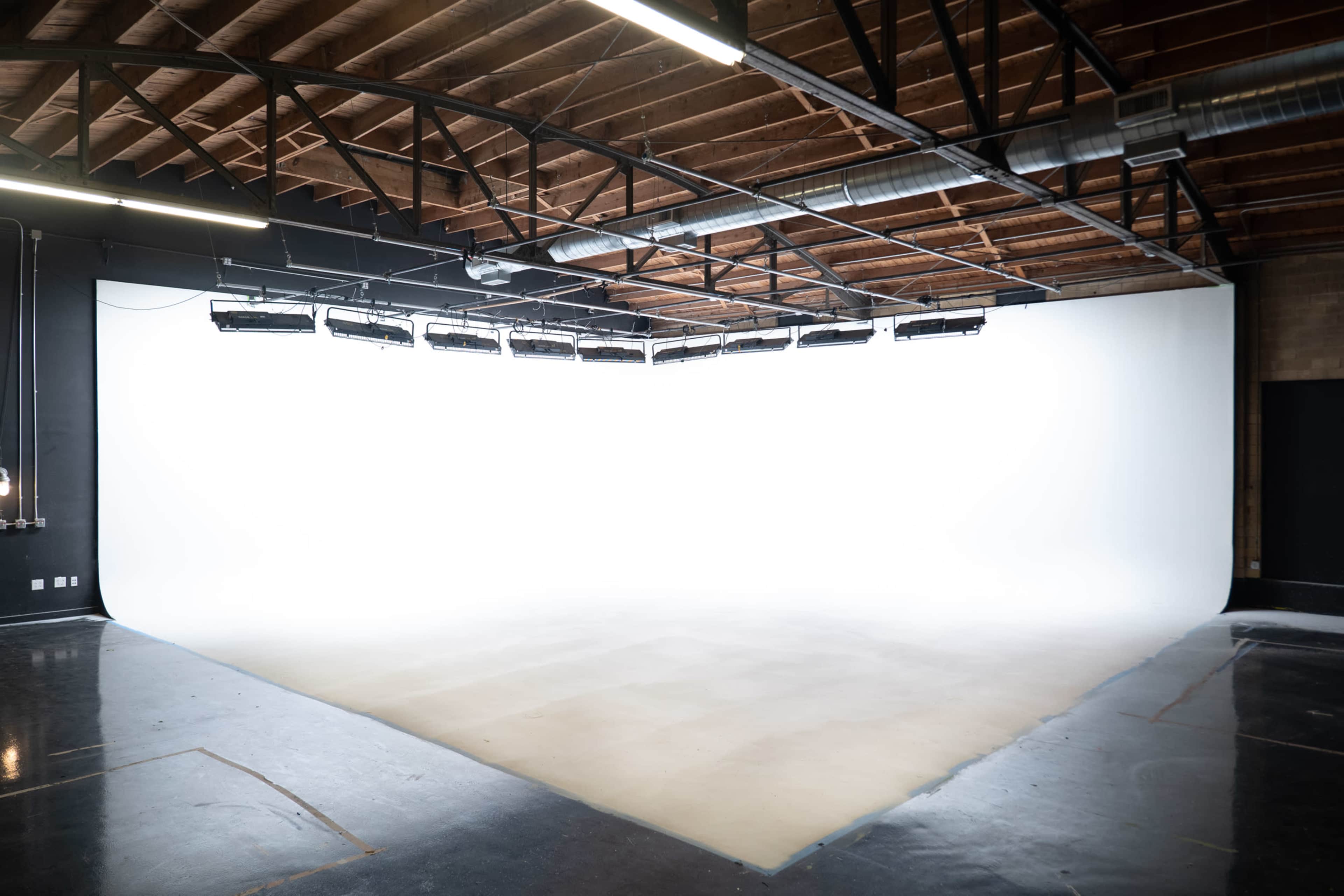 A spacious photography studio with a seamless white backdrop and a polished floor.