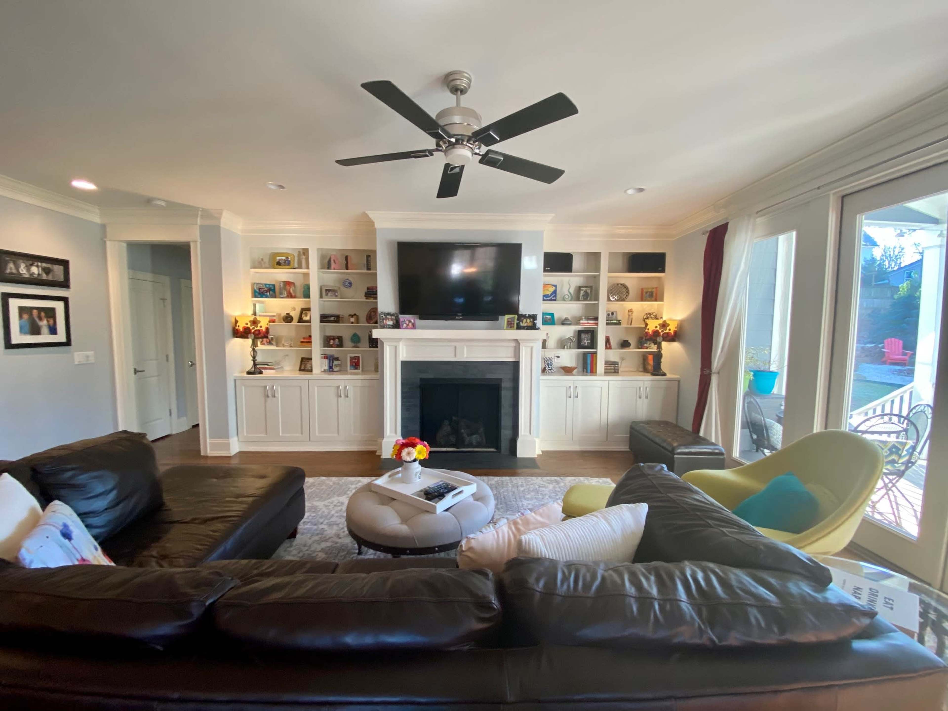The living room features a large sectional sofa, a television mounted above a fireplace, and built-in shelves displaying decorative items and photos.