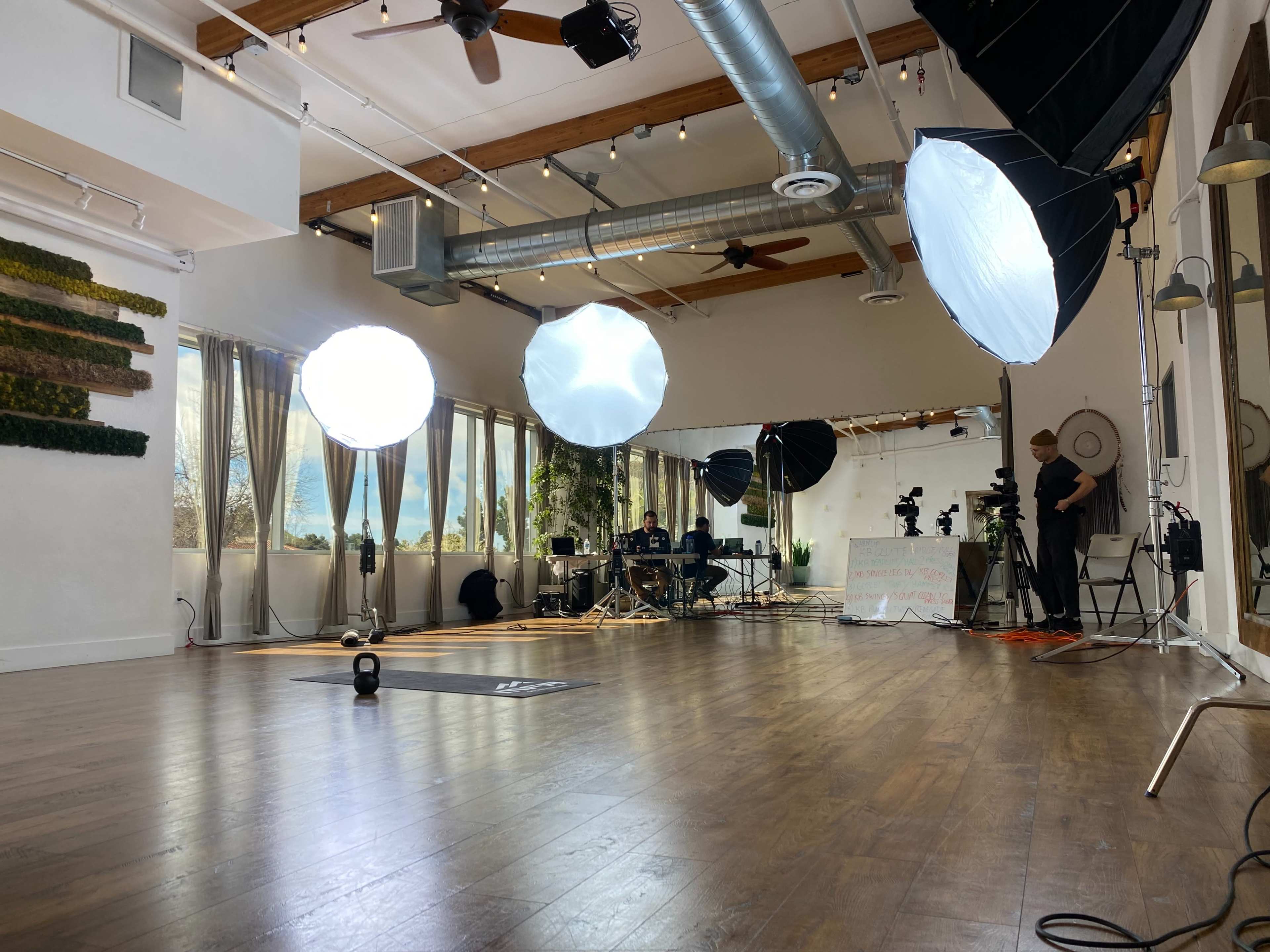 The image shows a spacious studio interior with several large softbox lights, a camera setup, and a band performing in the background.