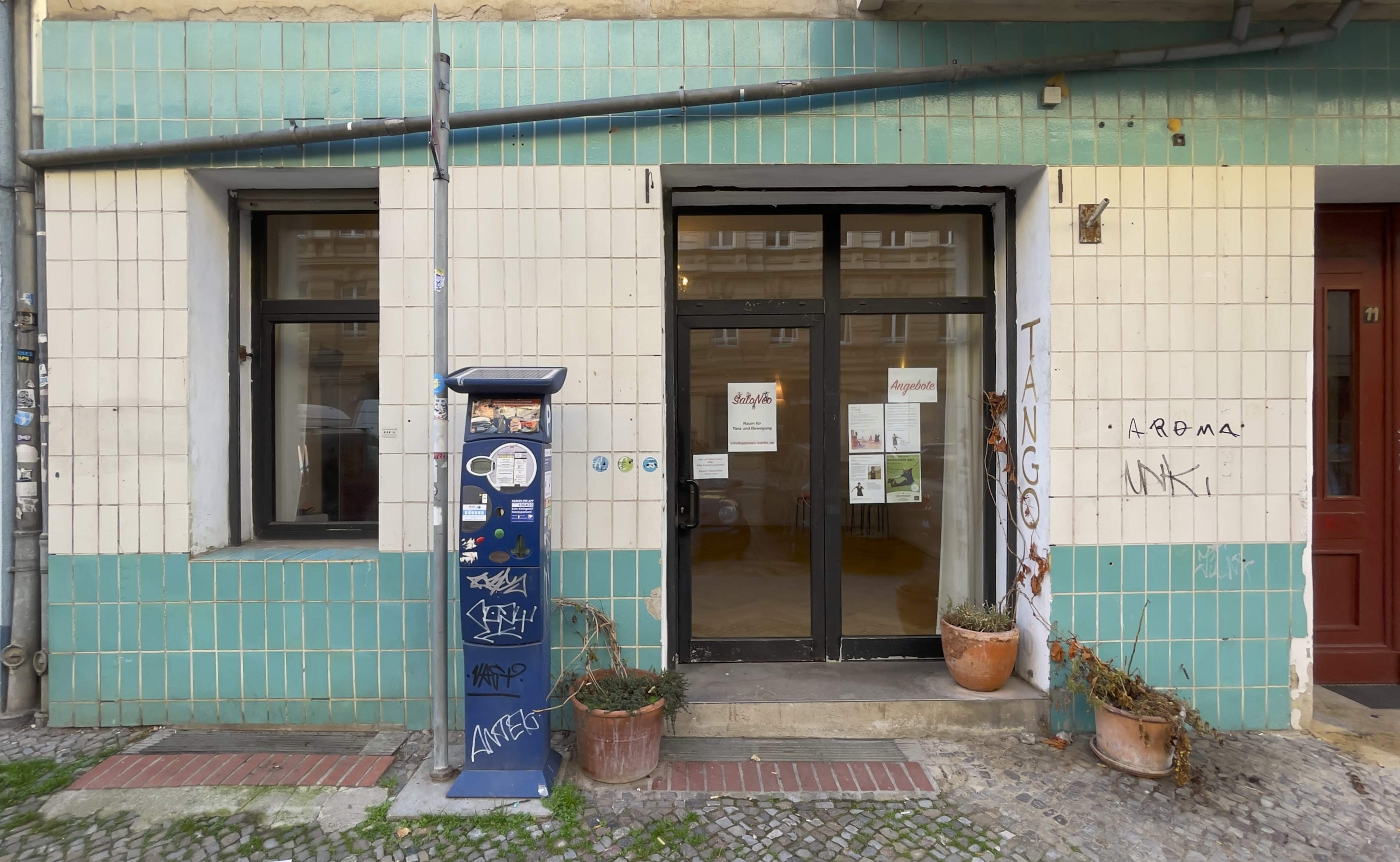 The entrance of a tiled shop front with a closed door, a mail box, and graffiti on the wall.