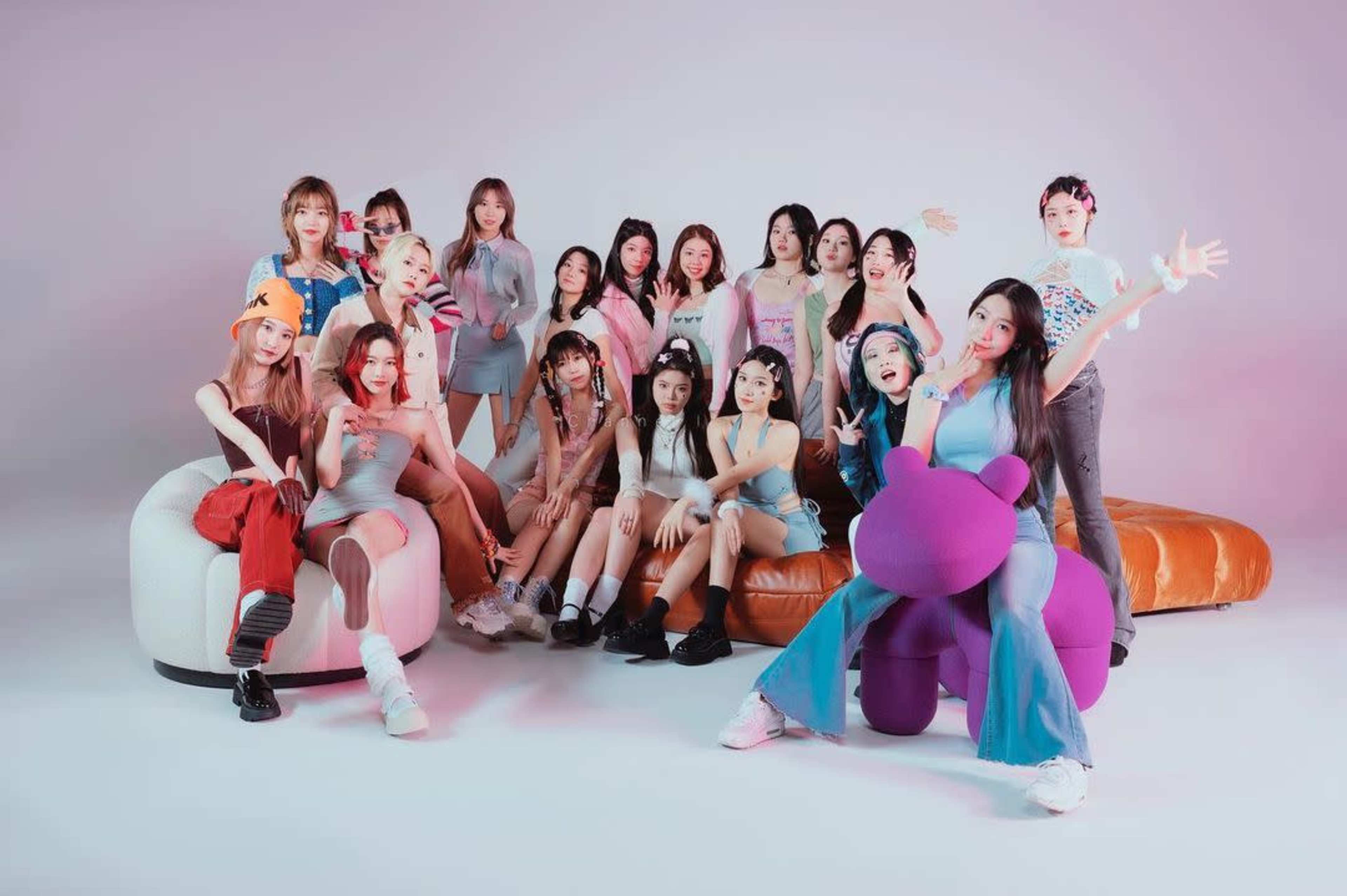 A group of young women poses together in a studio setting, sitting and standing around a large, colorful plush bear.