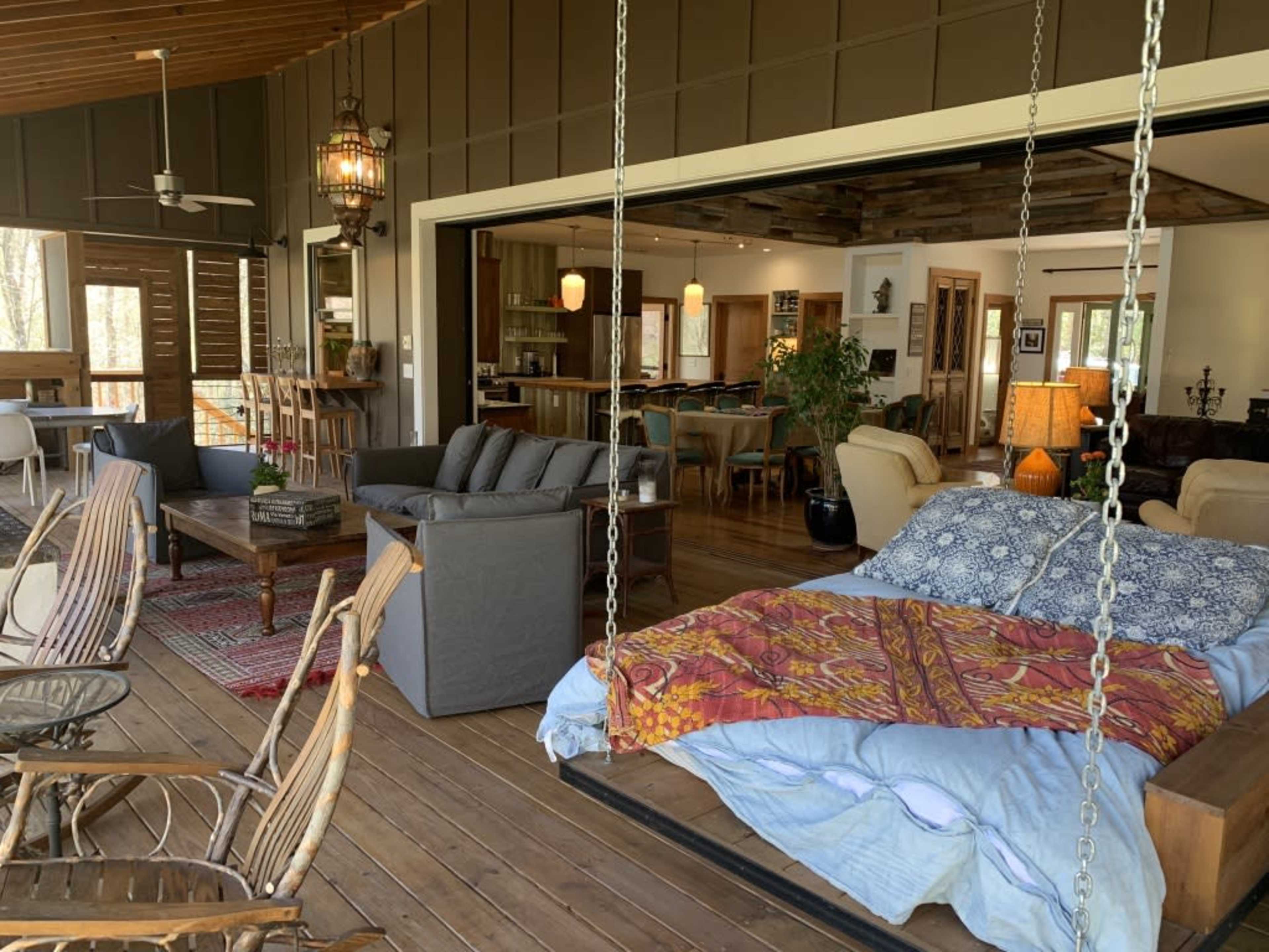 A cozy, open-concept living space with a hanging bed, comfortable seating, and a view of a dining area and kitchen in a rustic setting.