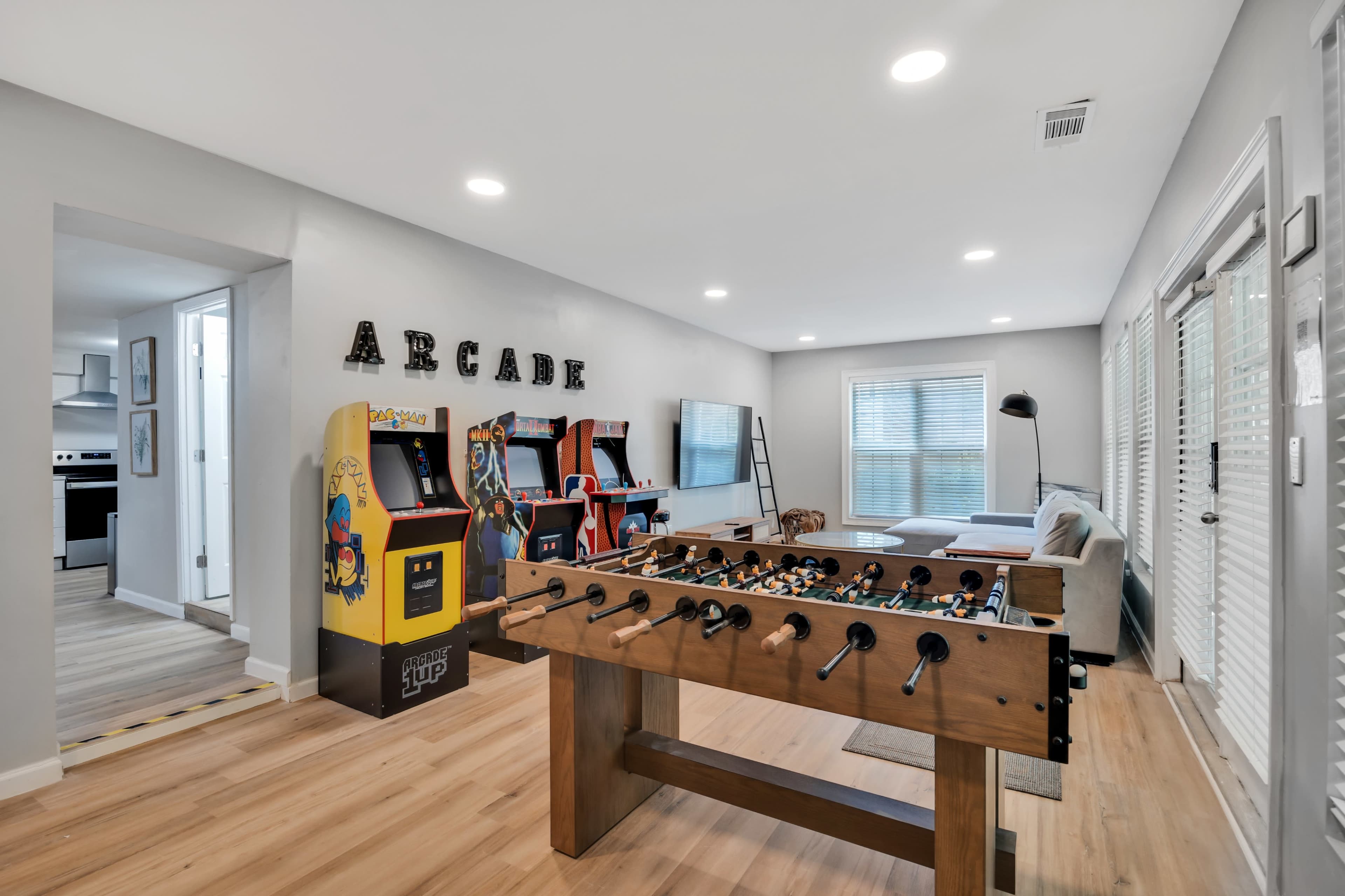 A modern game room featuring a foosball table, an arcade machine, and comfortable seating arranged near a large window.