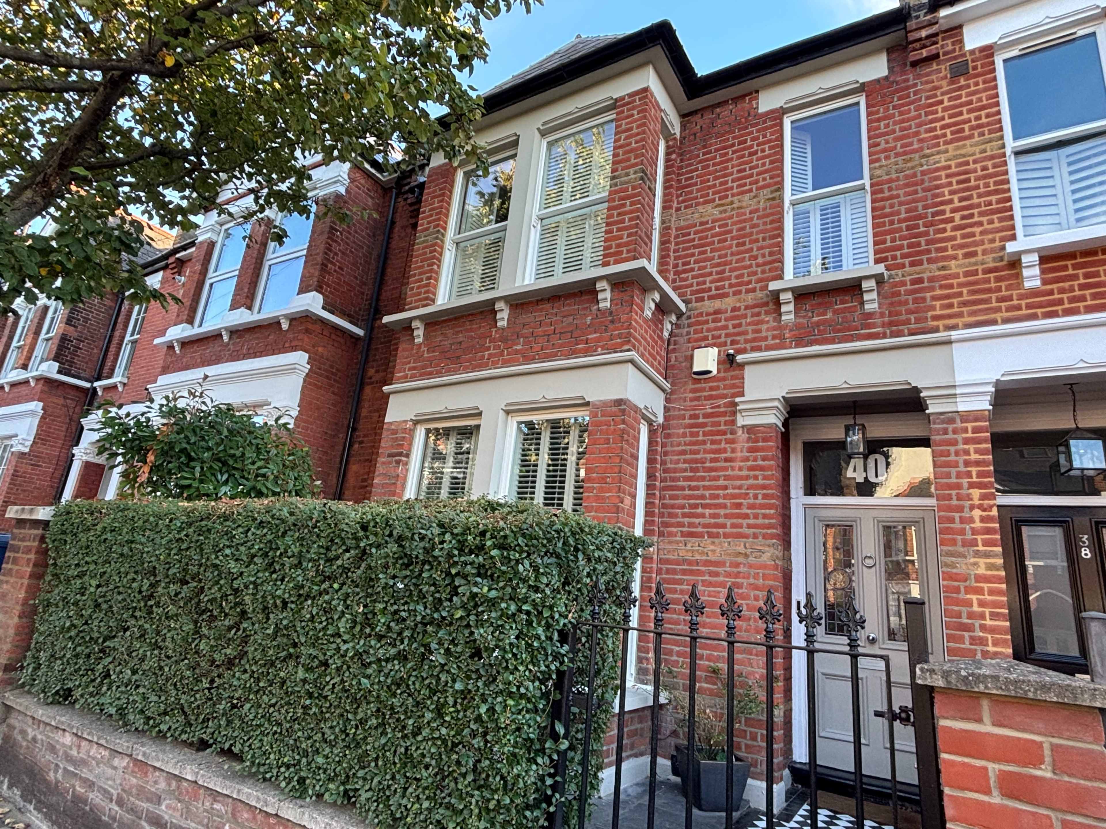 The image shows a two-story red brick house with white window frames and a small front garden enclosed by a black iron fence.