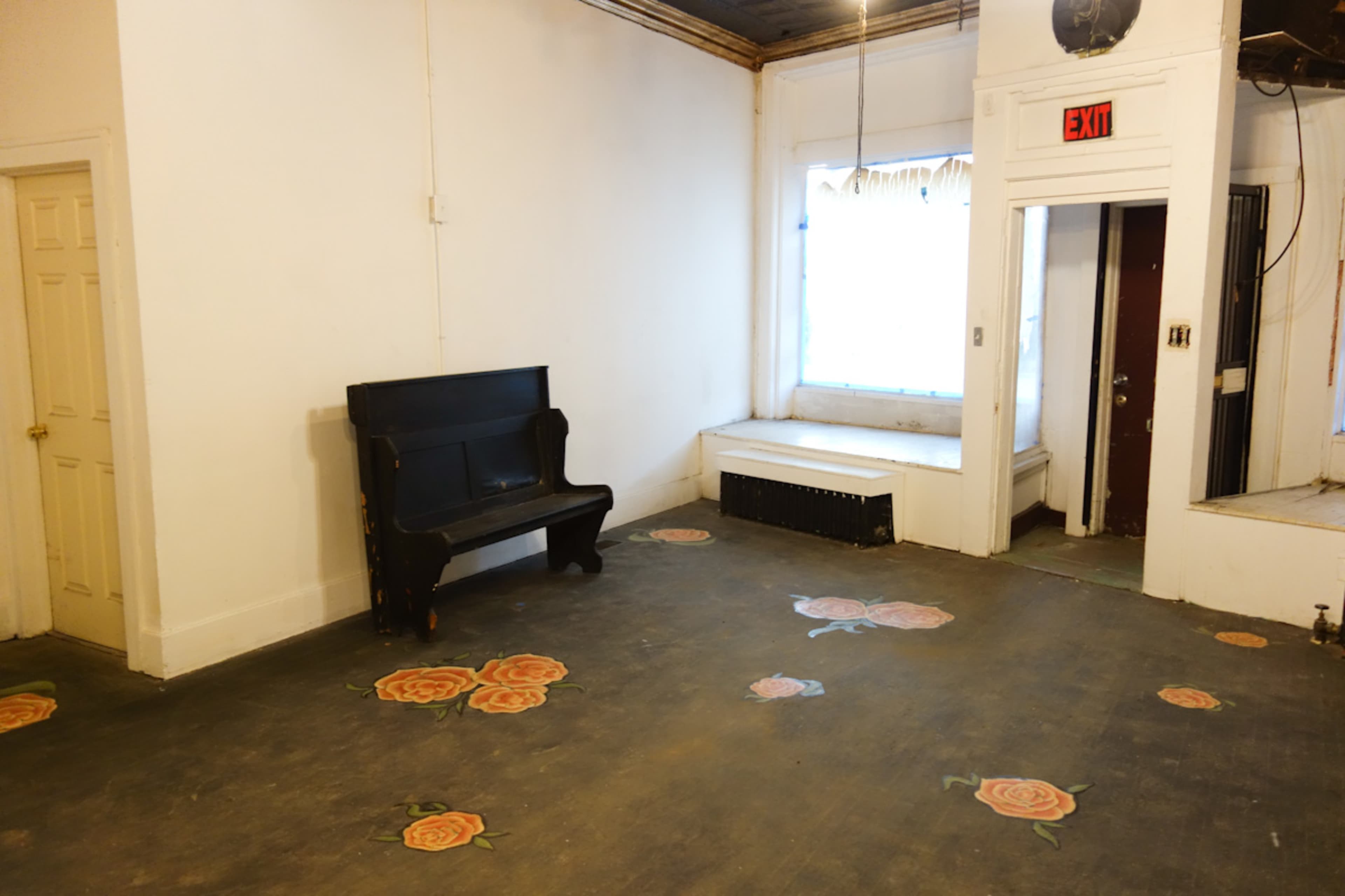The room features a black bench against a white wall, with floral designs on the floor and a large window illuminated by natural light.