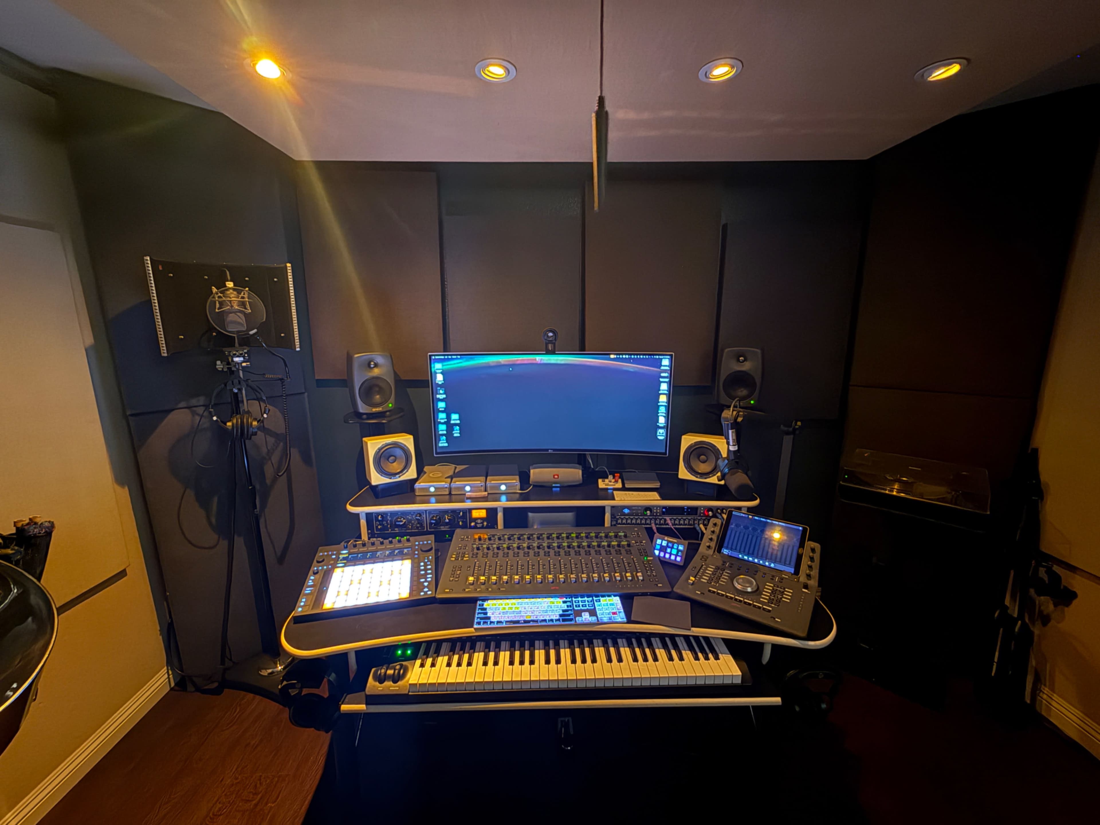 The image shows a modern music production studio setup with a computer, audio equipment, speakers, and a MIDI keyboard arranged on a desk.
