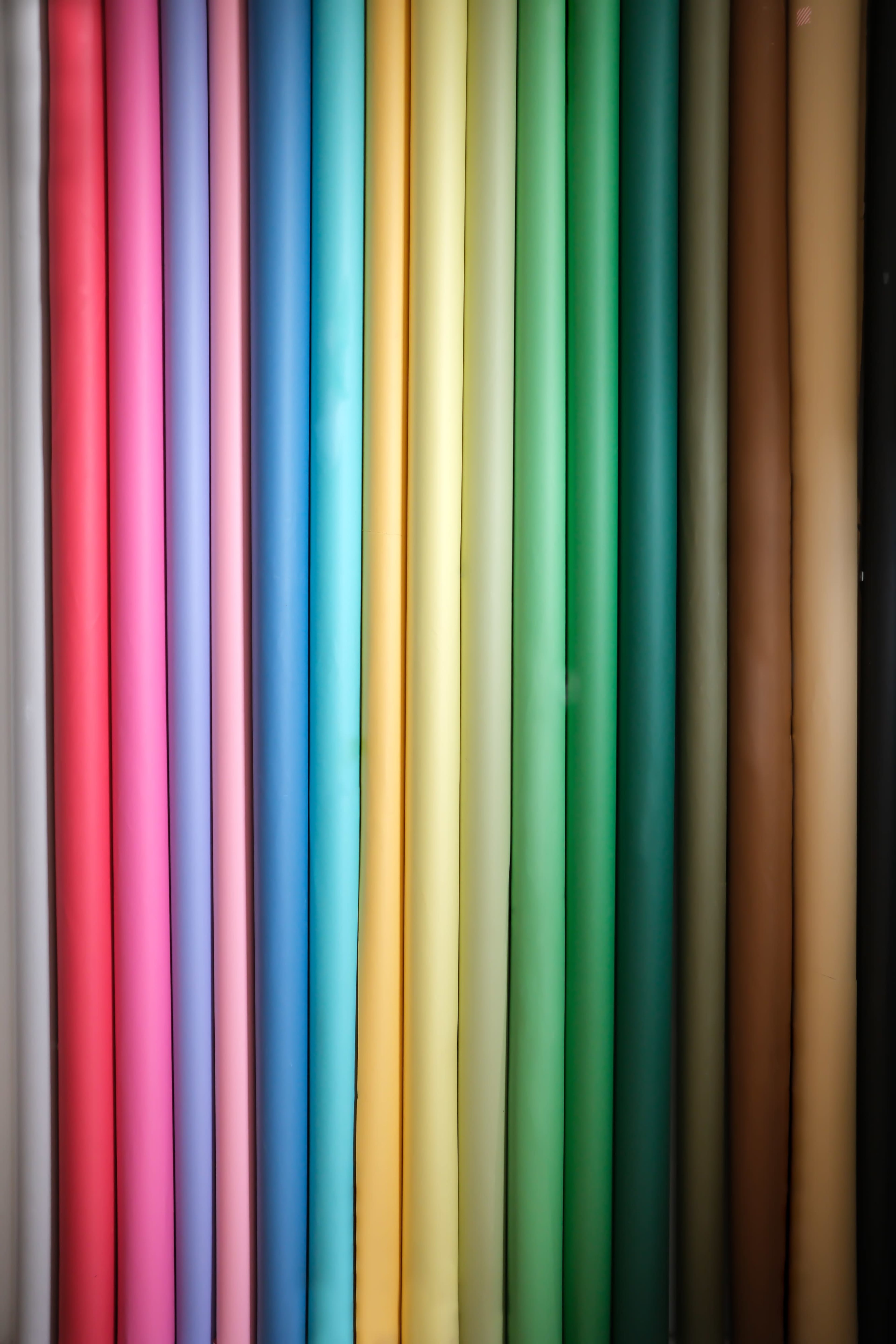 The image shows a vertical arrangement of rolled sheets in various colors, including pink, blue, green, yellow, and brown.