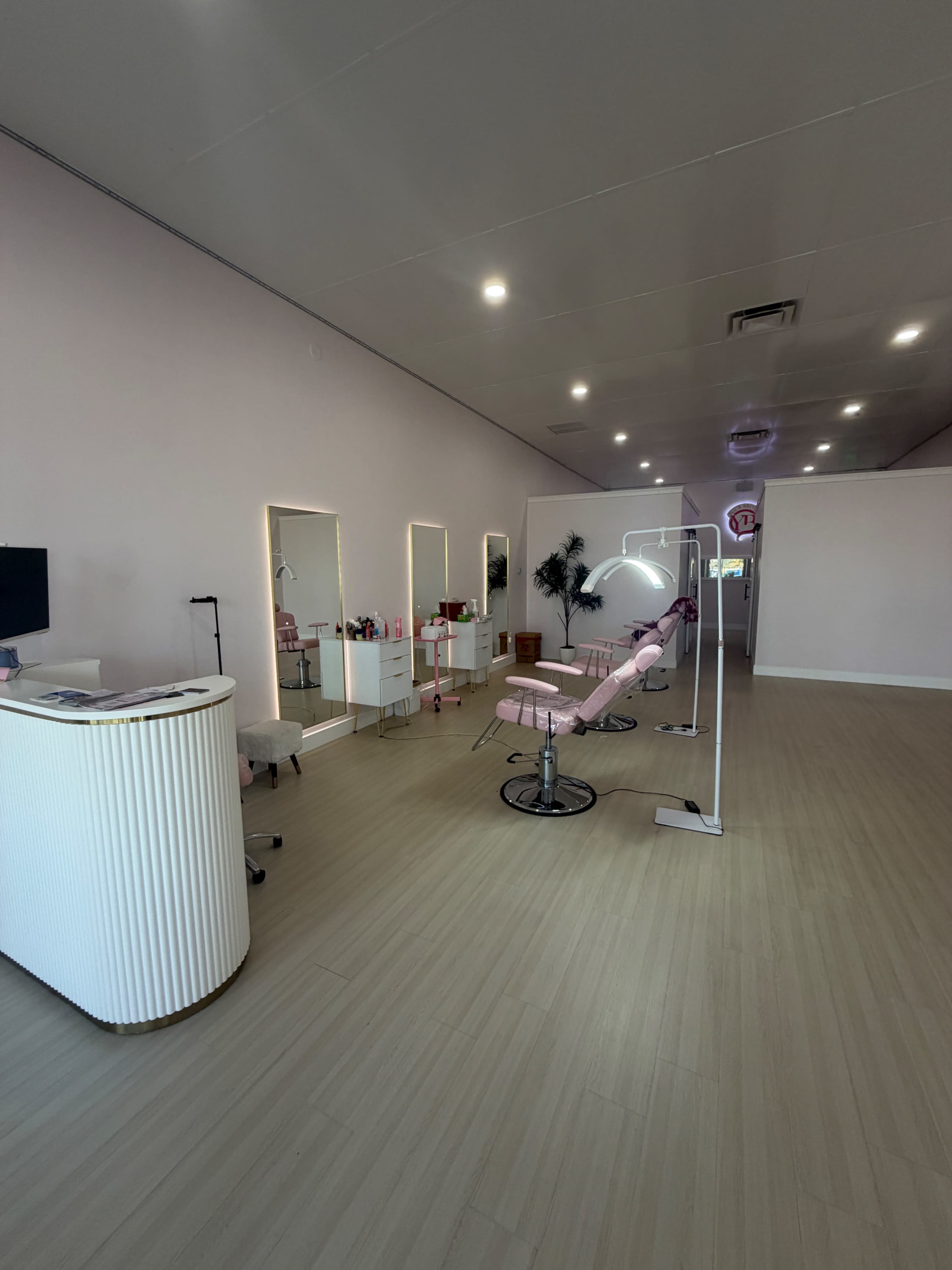 The image shows a modern beauty salon interior with pink accents, a treatment chair, mirrors, and well-organized furniture.