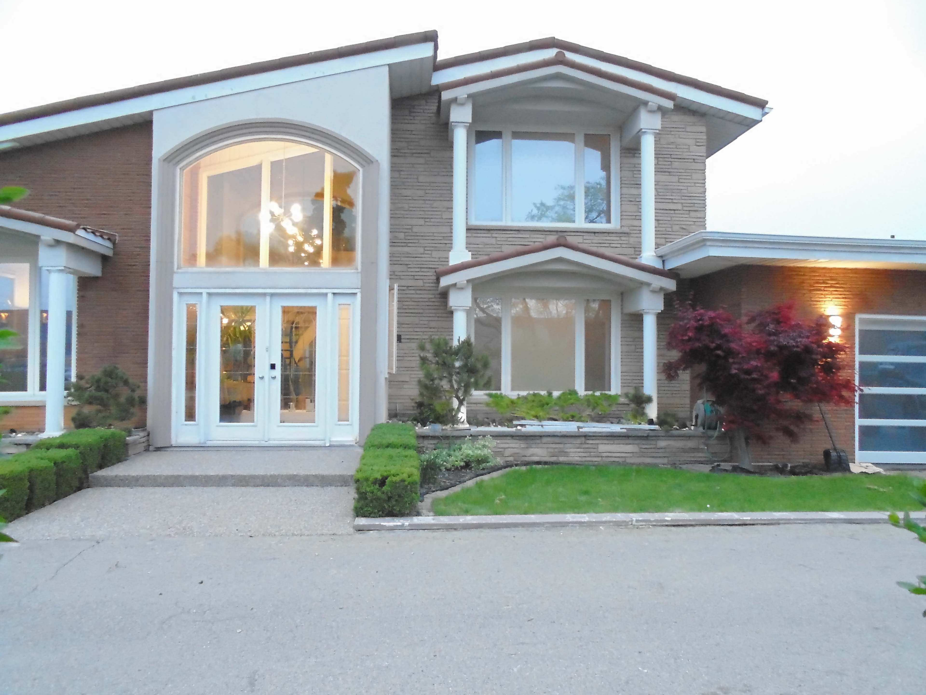 A modern two-story house with a large front entrance, a neatly landscaped yard, and large windows.