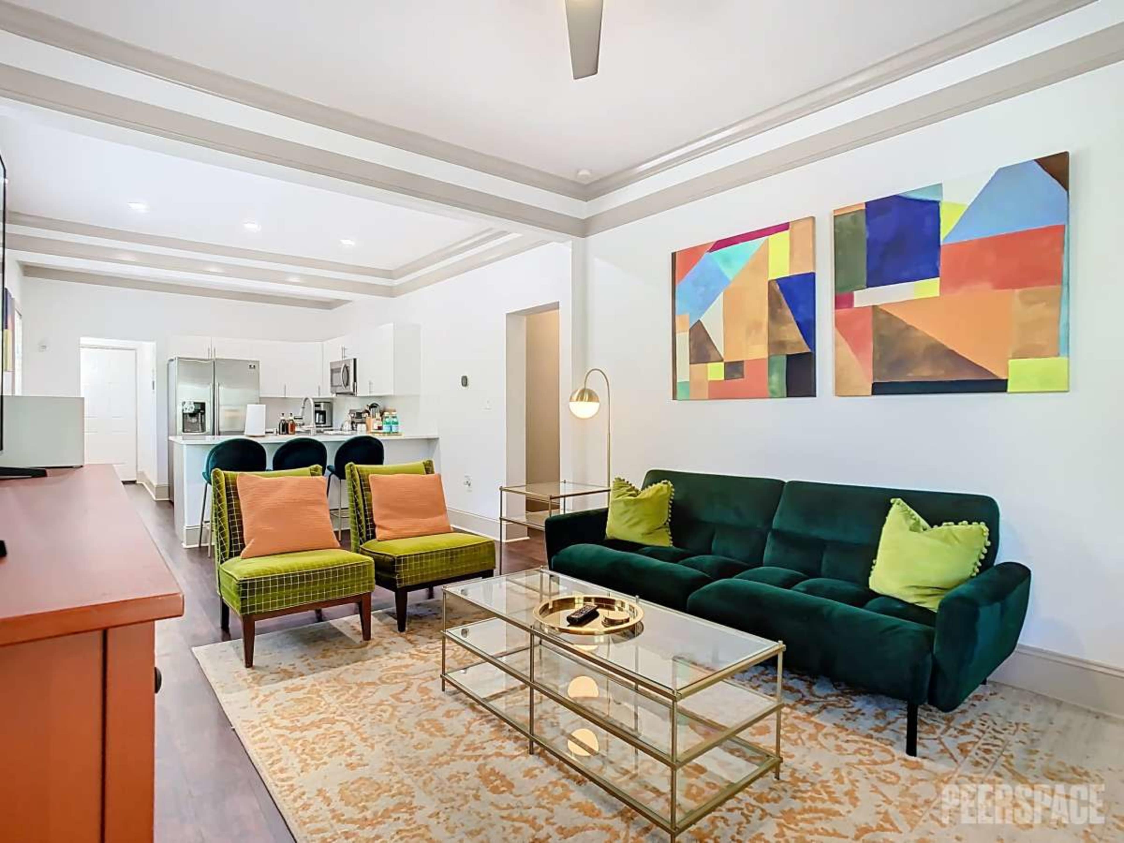 The image shows a modern living room featuring a green sofa, two yellow armchairs, a glass coffee table, and abstract artwork on the wall.