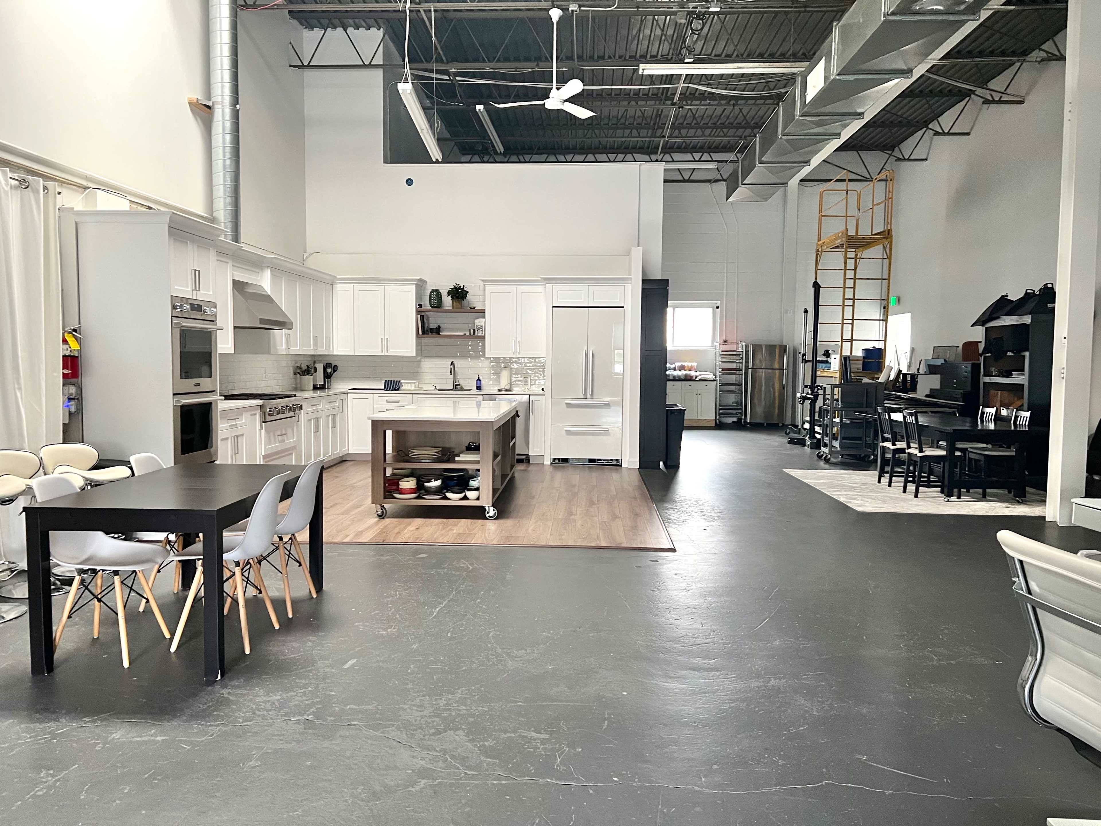 A spacious kitchen and dining area within a modern industrial-style room featuring white cabinetry, a large island, and a dining table with chairs.