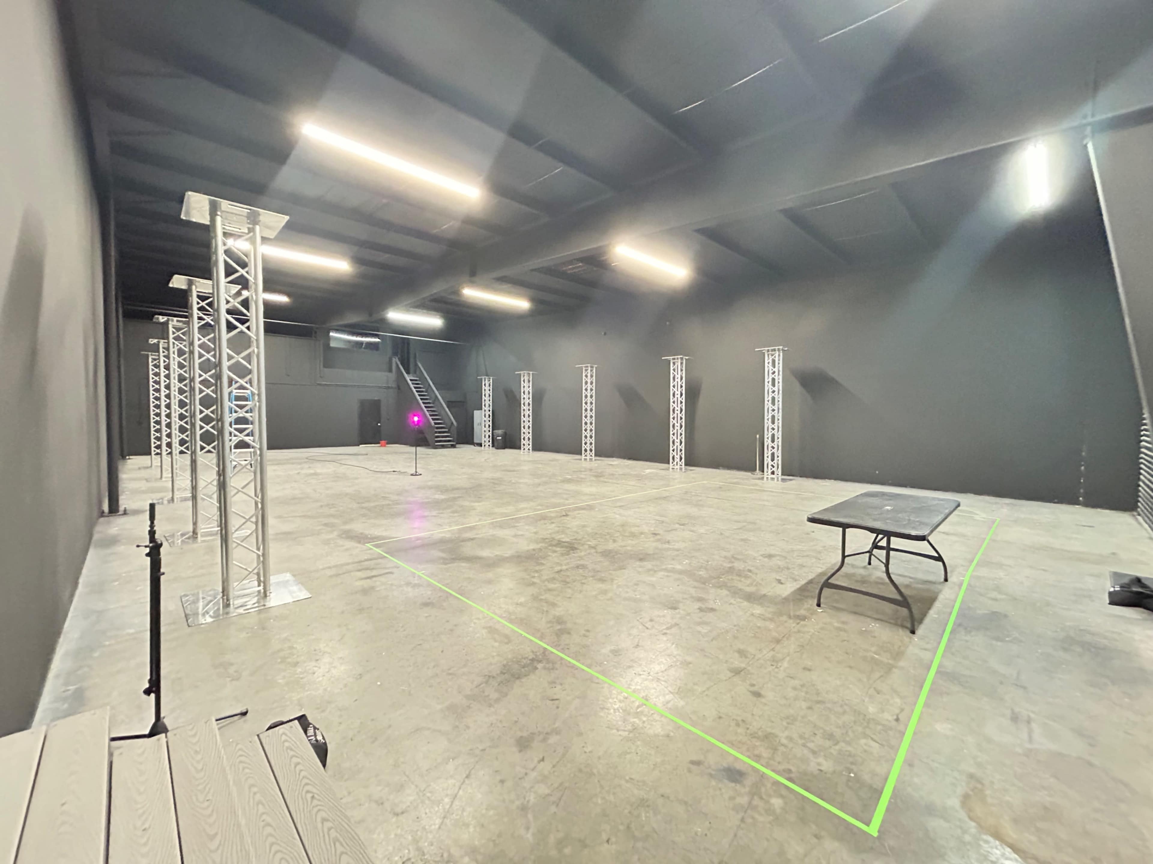 An empty studio space with metal truss structures positioned around a concrete floor, illuminated by overhead lights.