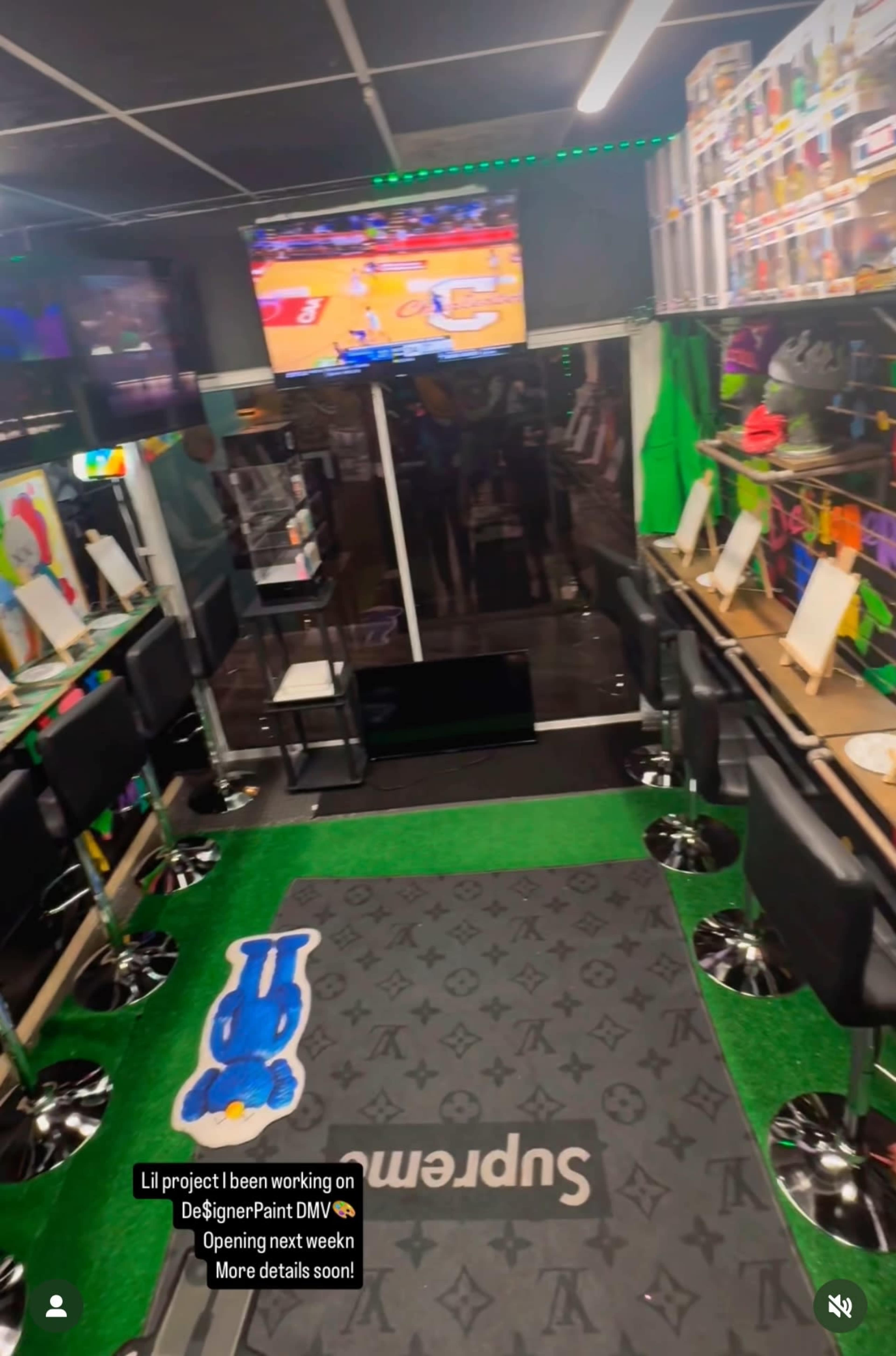 The image shows an interior space designed for a business, featuring black bar stools, a gaming area with a television displaying a sports game, and various items on display along the walls.