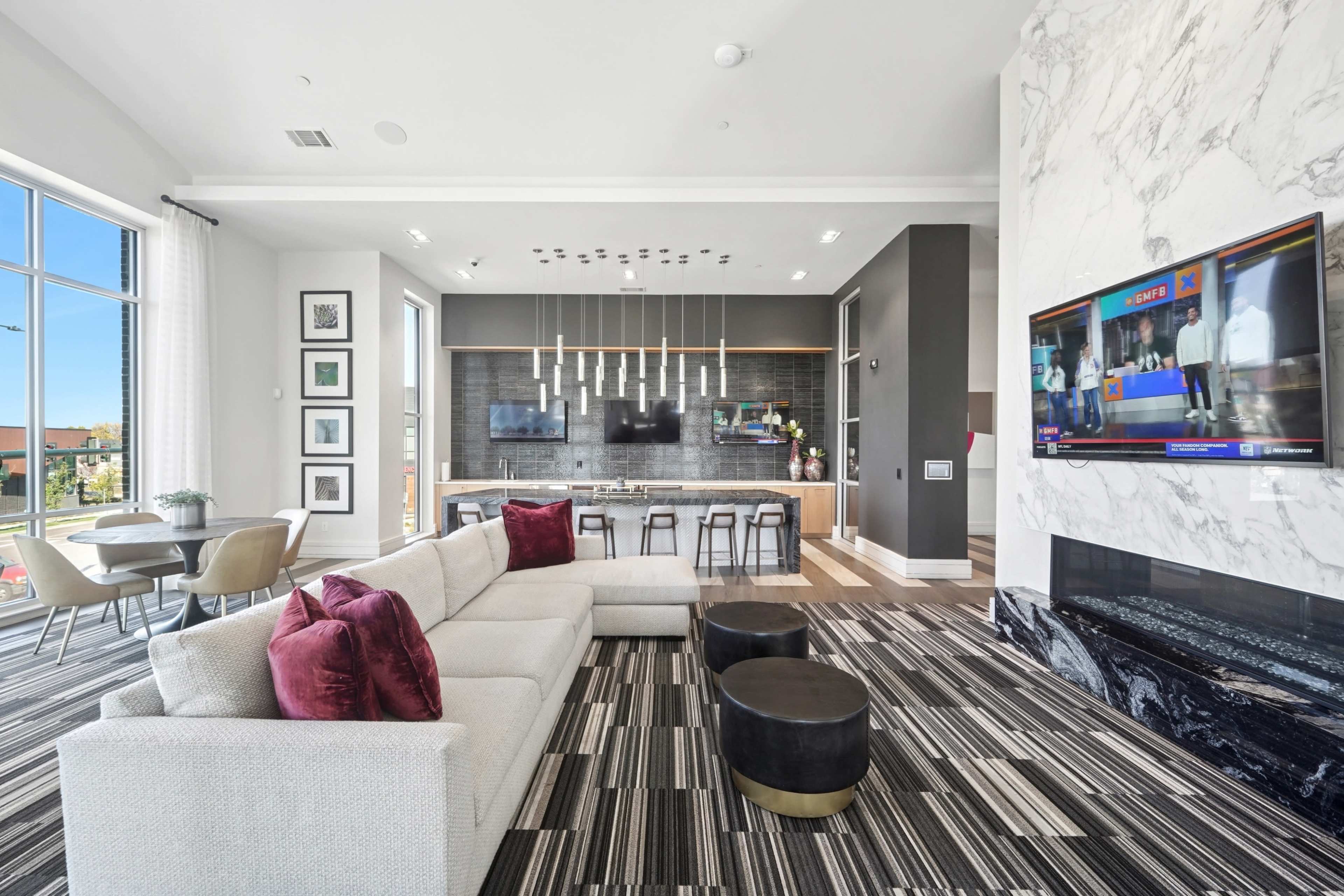 A modern living area features a sleek sofa, a round dining table, and a kitchen with bar seating, all set against a backdrop of large windows and a marble accent wall.