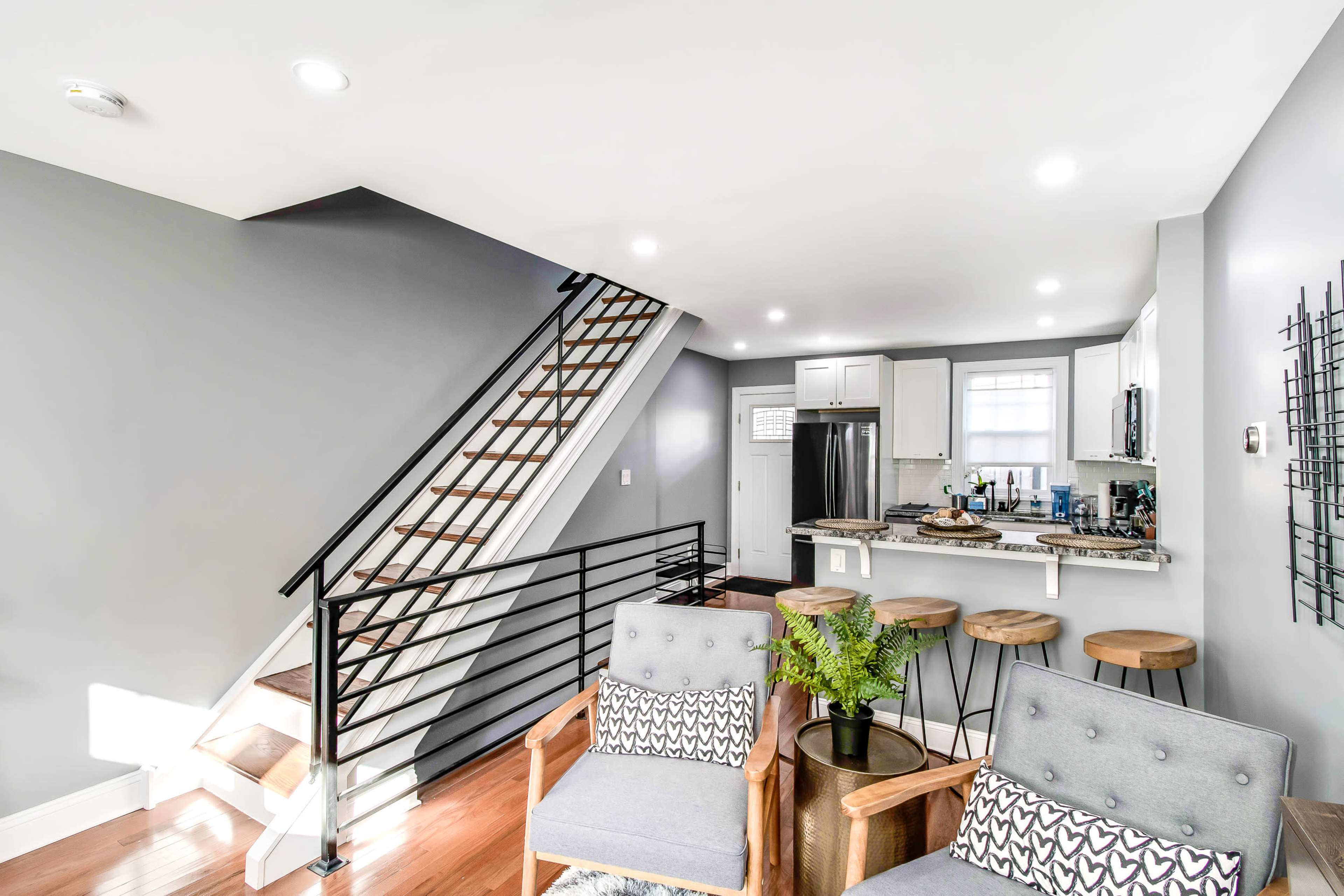 The image features a modern interior with a staircase, a kitchen area, and seating arranged in a living space.