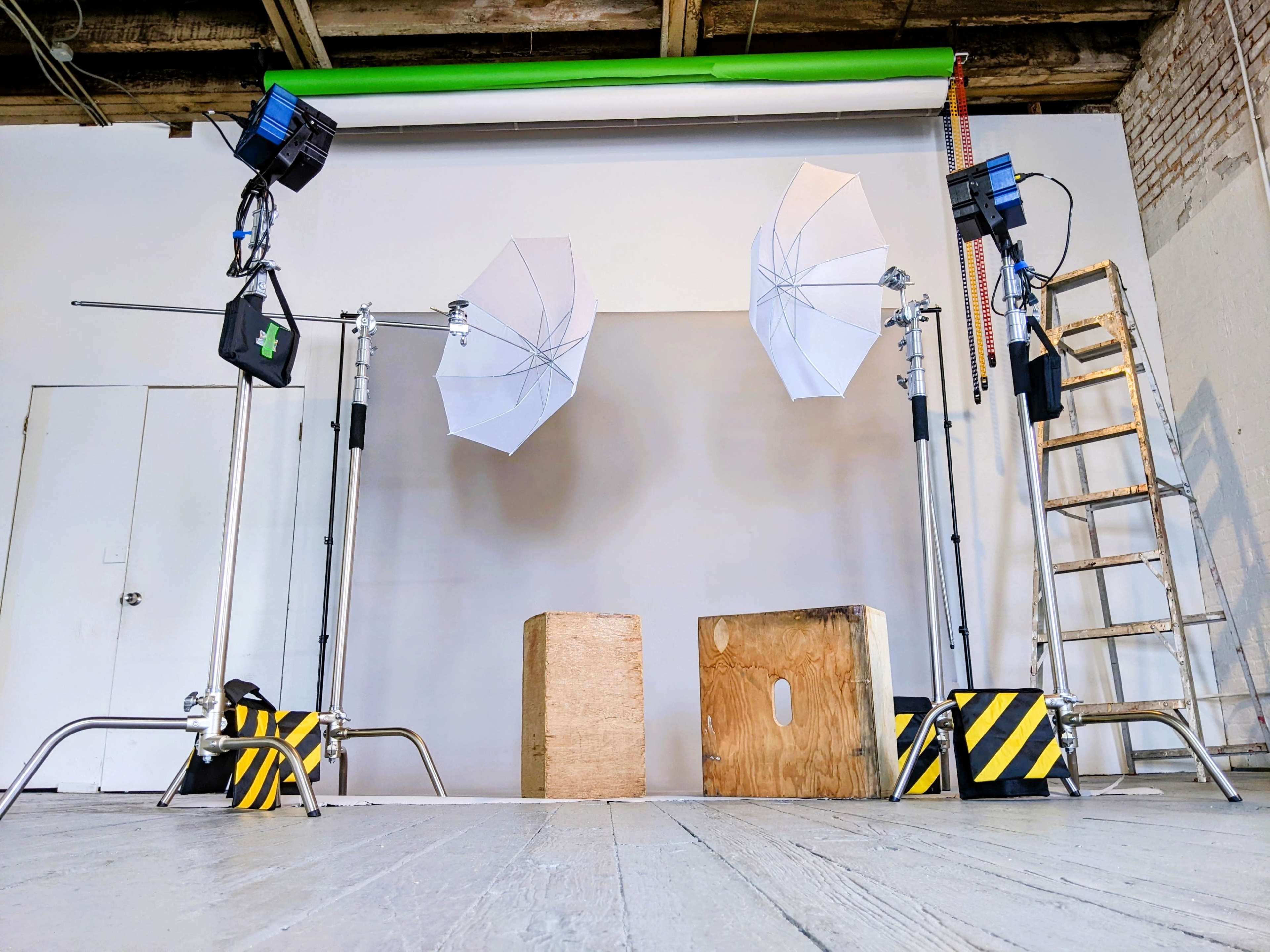 A photography studio setup with two softbox lights, a backdrop, two wooden blocks, and a ladder against a brick wall.