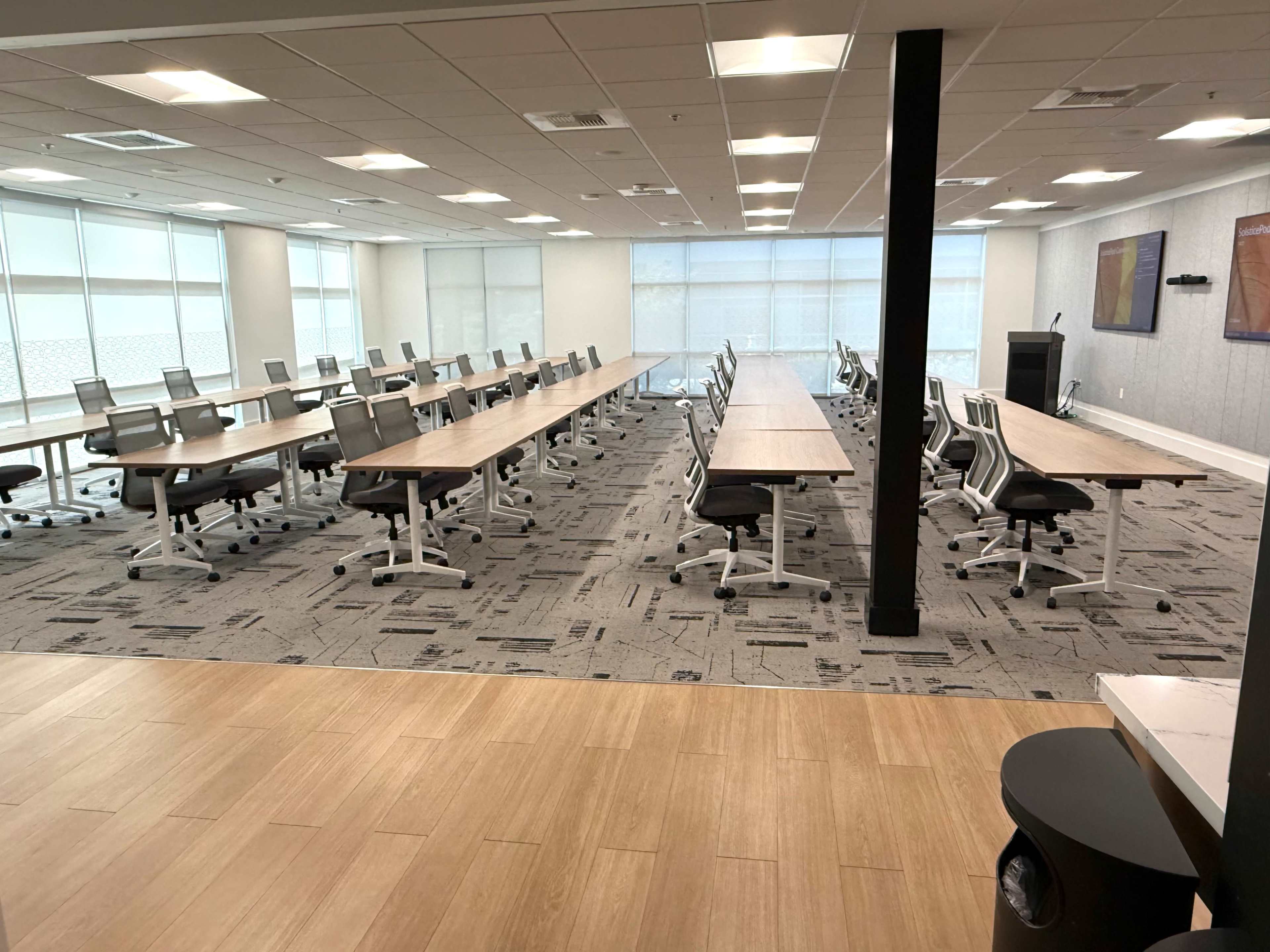 The image shows a spacious, empty conference room with several long tables arranged in a grid and adjustable office chairs.