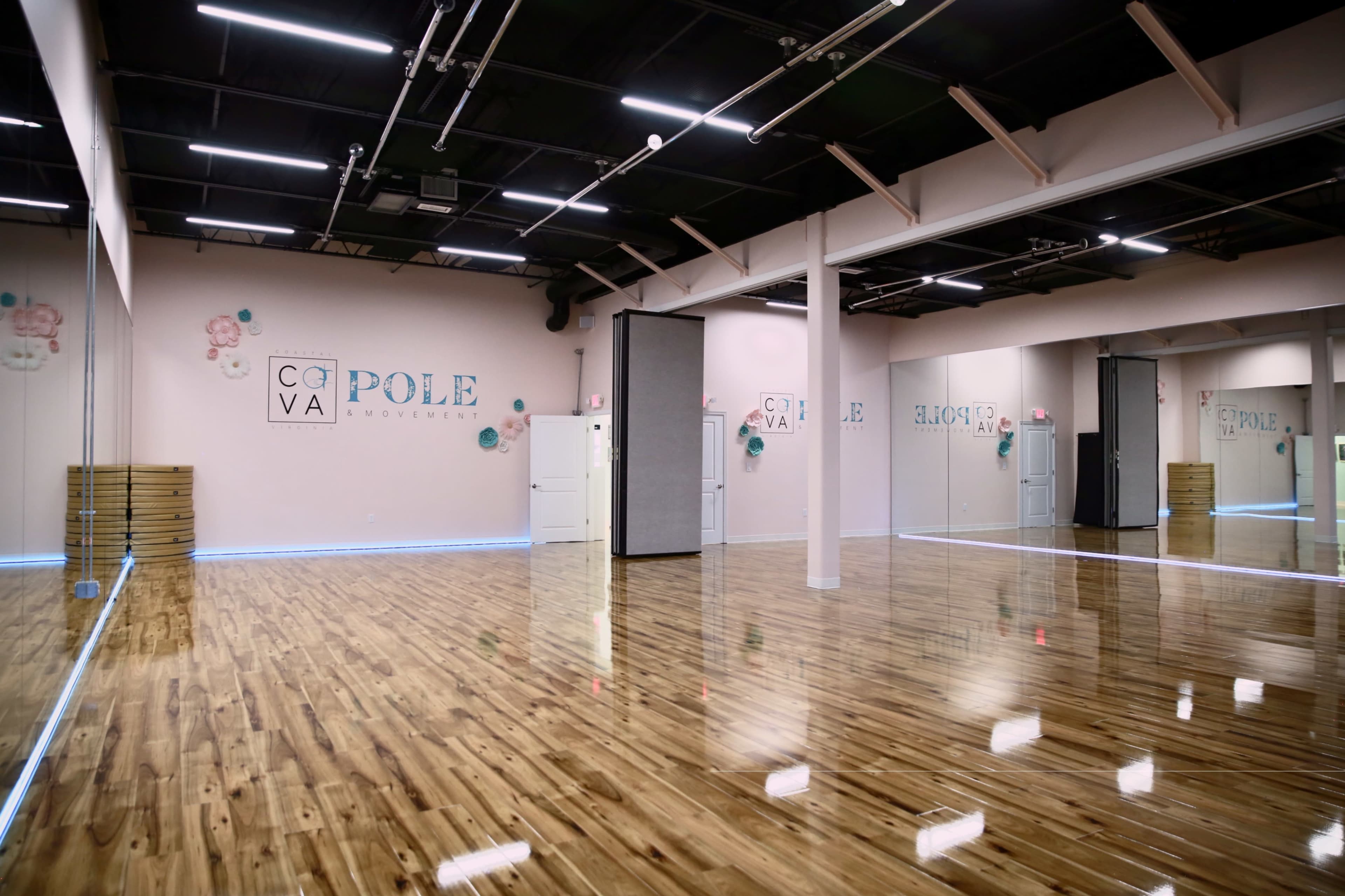 The image shows a spacious, wood-floored studio with mirrors, soft lighting, and decorated walls.