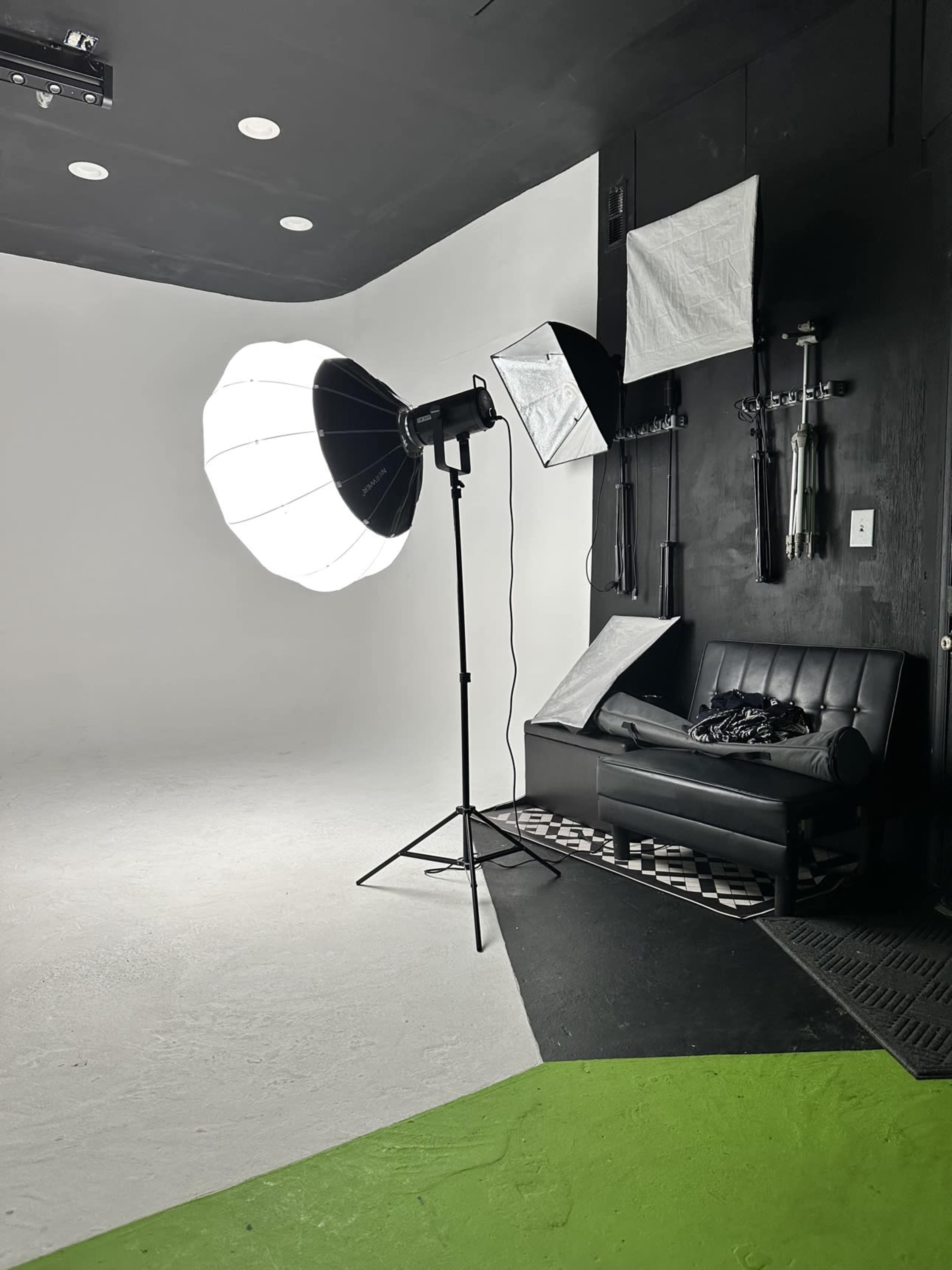 The image shows a photography studio with a large softbox light, a black couch, and various studio equipment mounted on the wall.