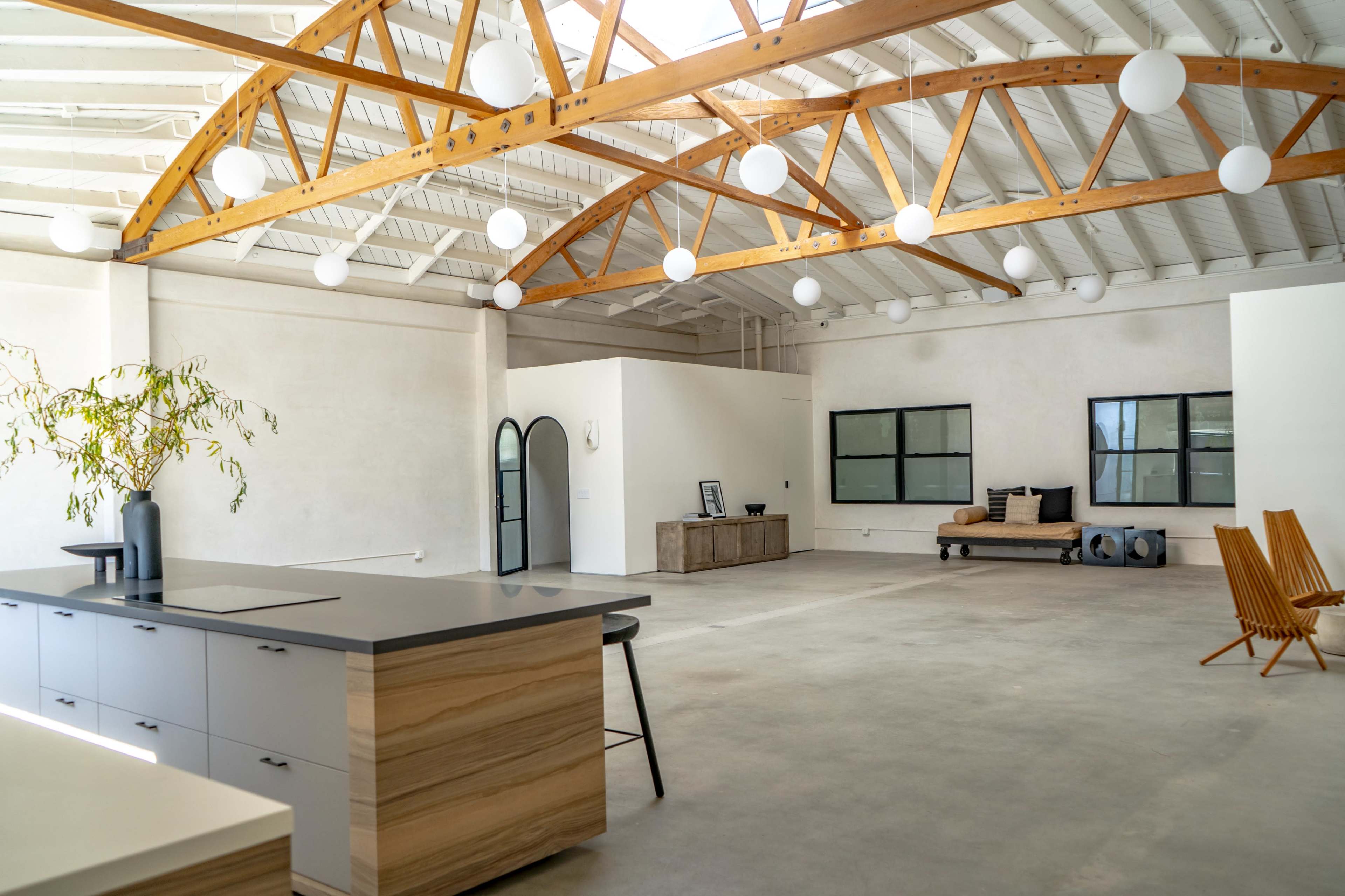 A spacious, modern interior with high ceilings, exposed wooden beams, and a minimalist kitchen area featuring an island and sleek cabinetry.