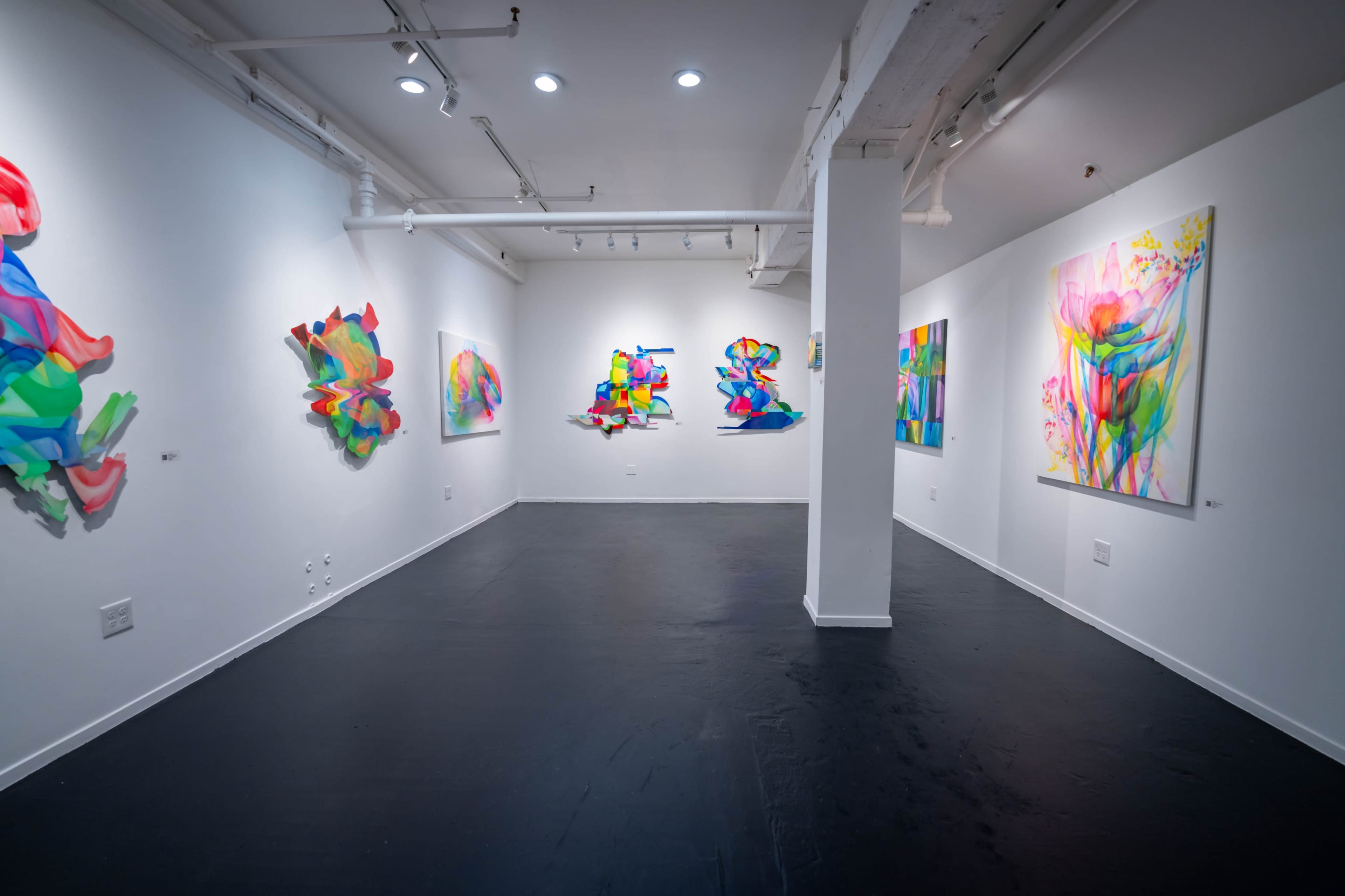 An art gallery with colorful abstract paintings and sculptures displayed on the white walls.