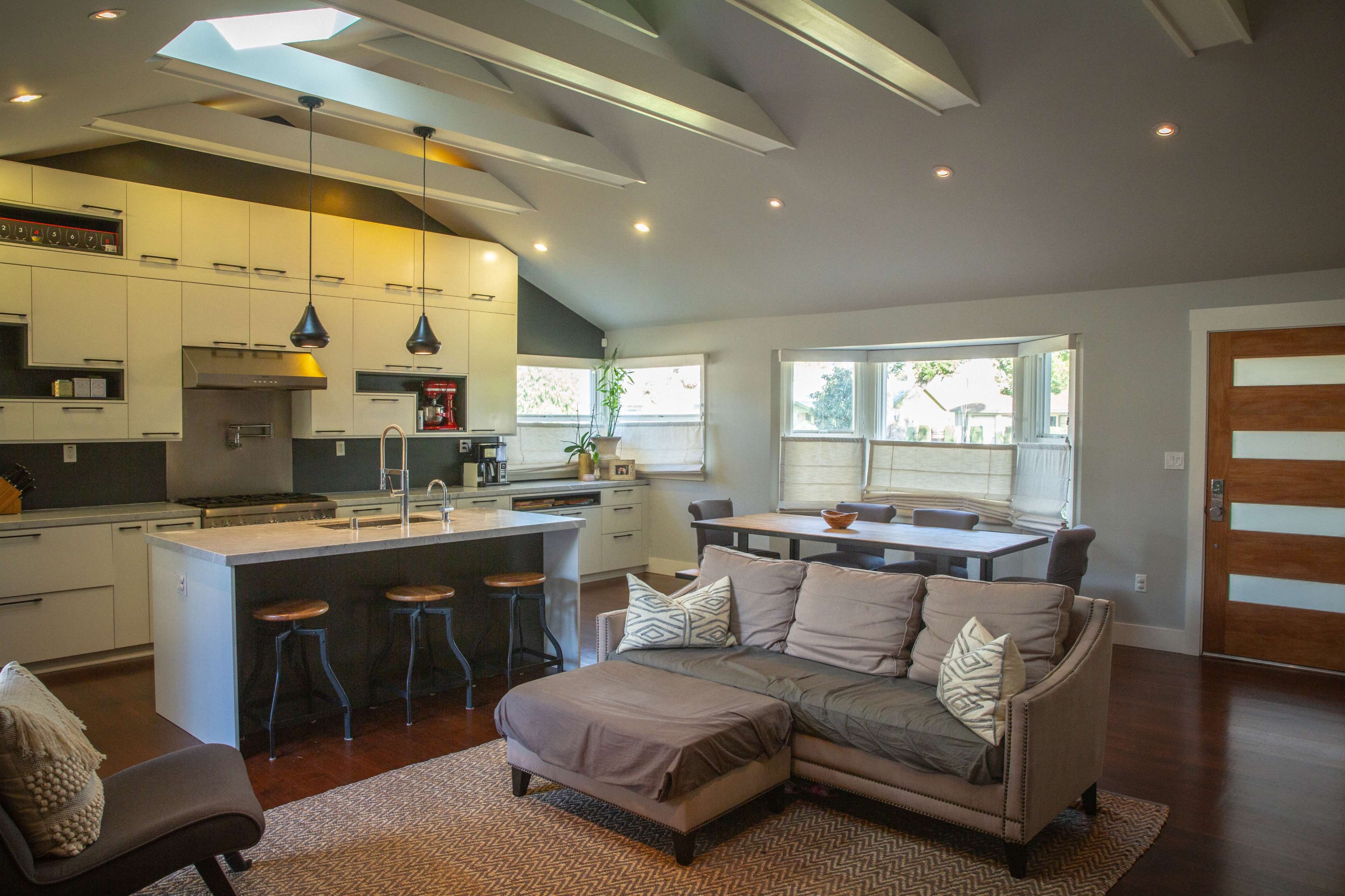 A modern open-concept kitchen and living area with a sectional sofa, a dining table, and large windows allowing natural light.