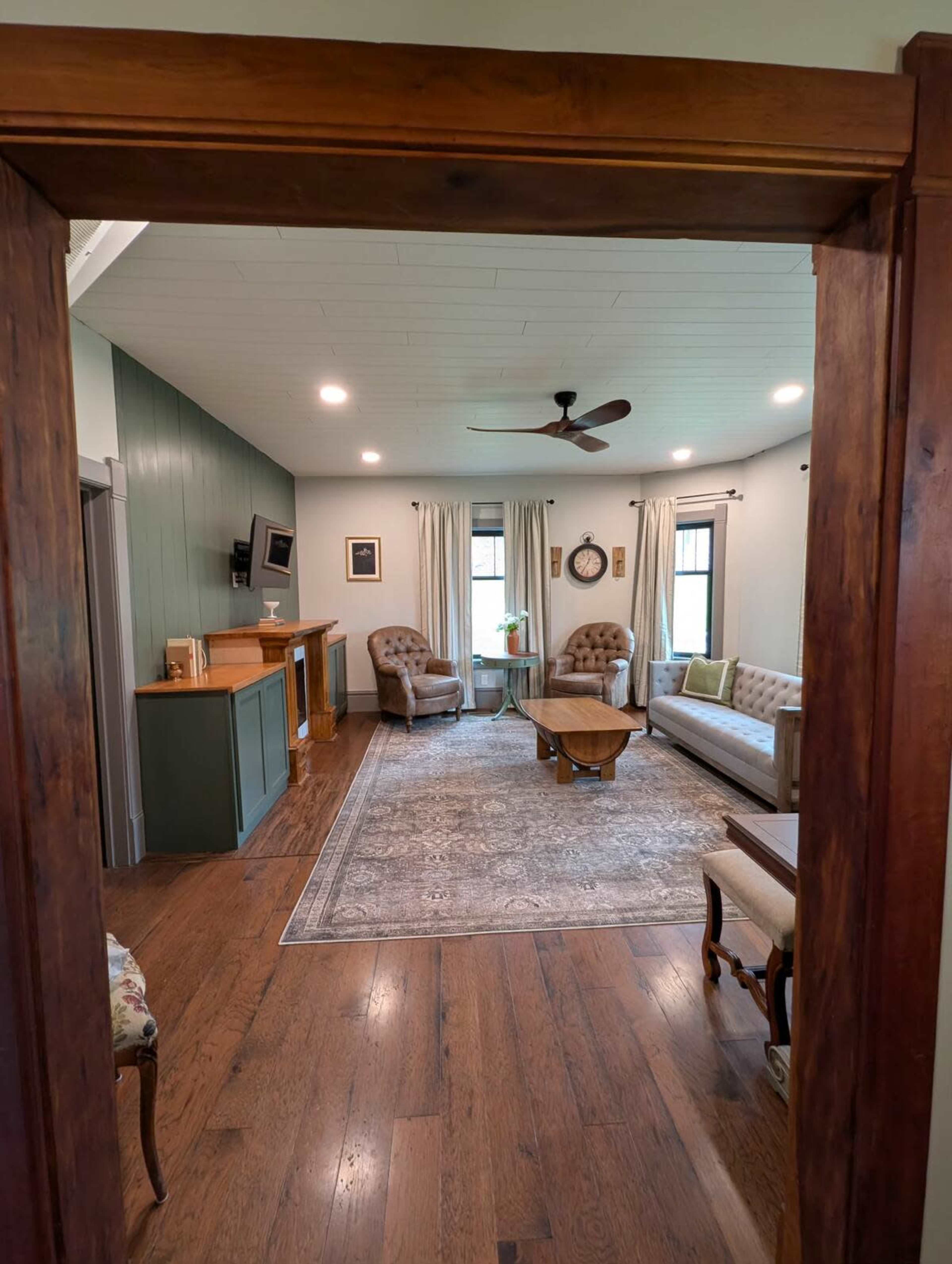 The image shows a cozy living room with two armchairs, a coffee table, and a large area rug, framed by a doorway featuring wooden trim.