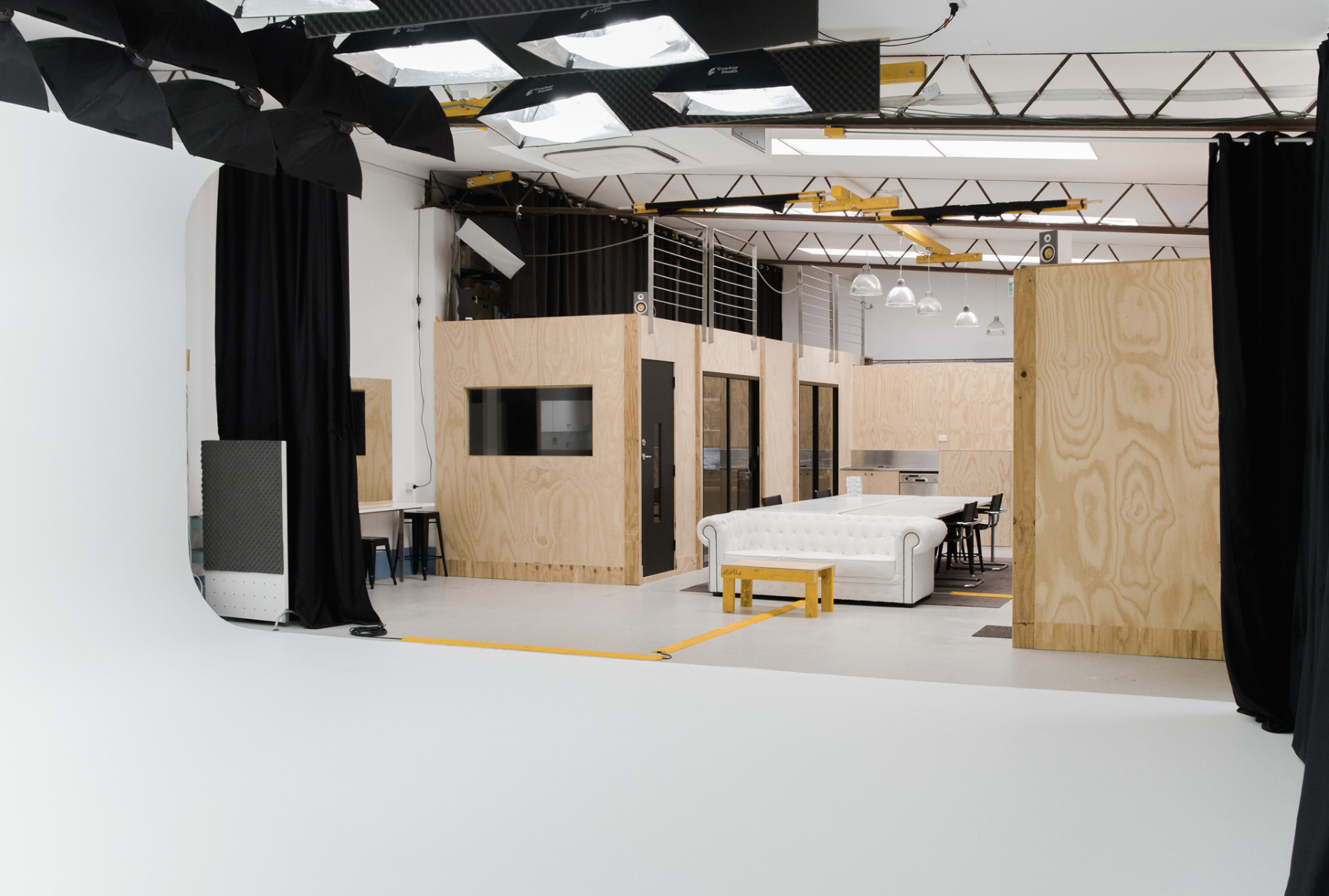 The image shows a spacious studio interior featuring wooden partitions, a white couch, and studio lighting equipment.