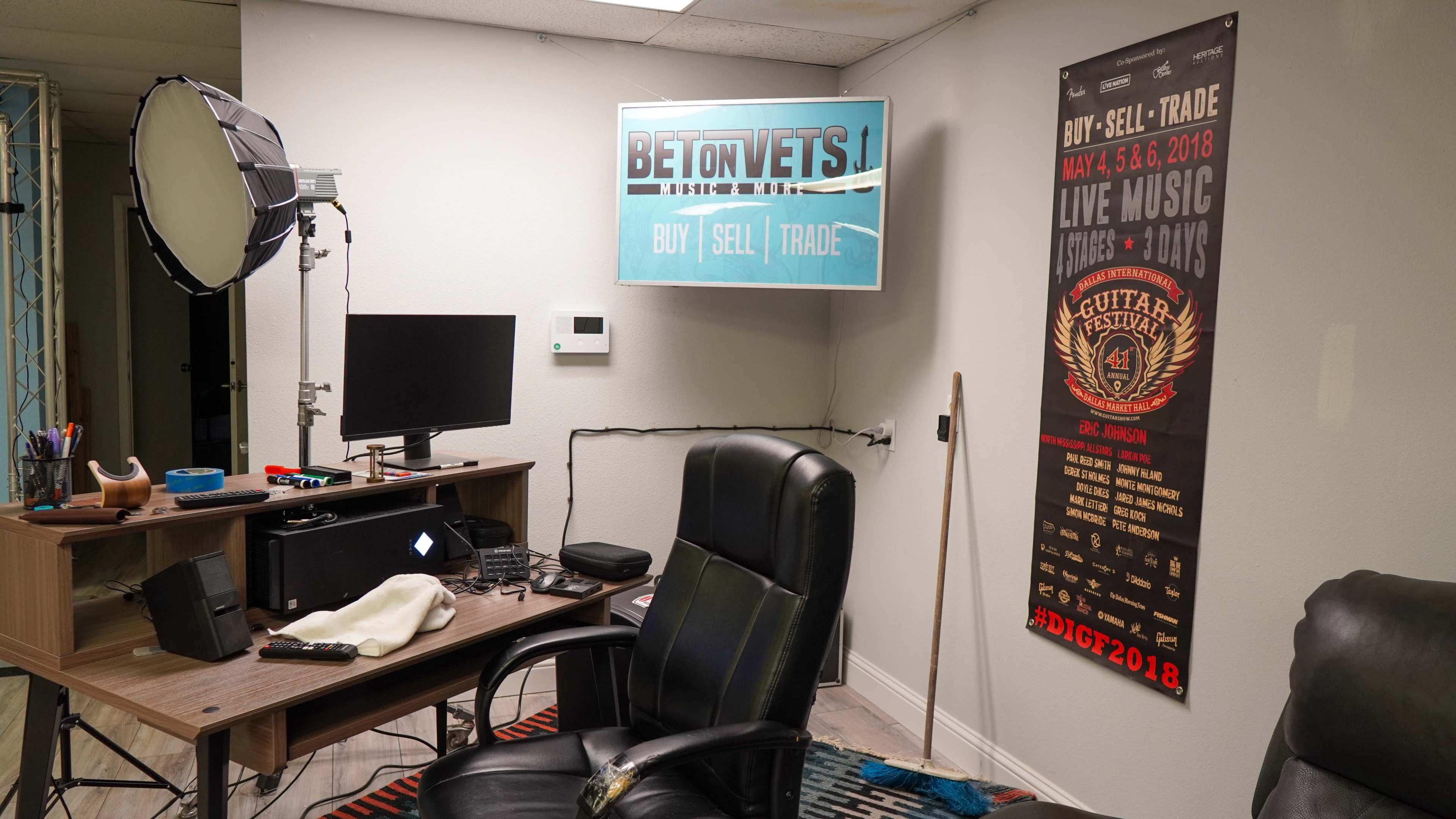 A small office space with a desk, computer monitor, and a poster advertising a live music event on the wall.
