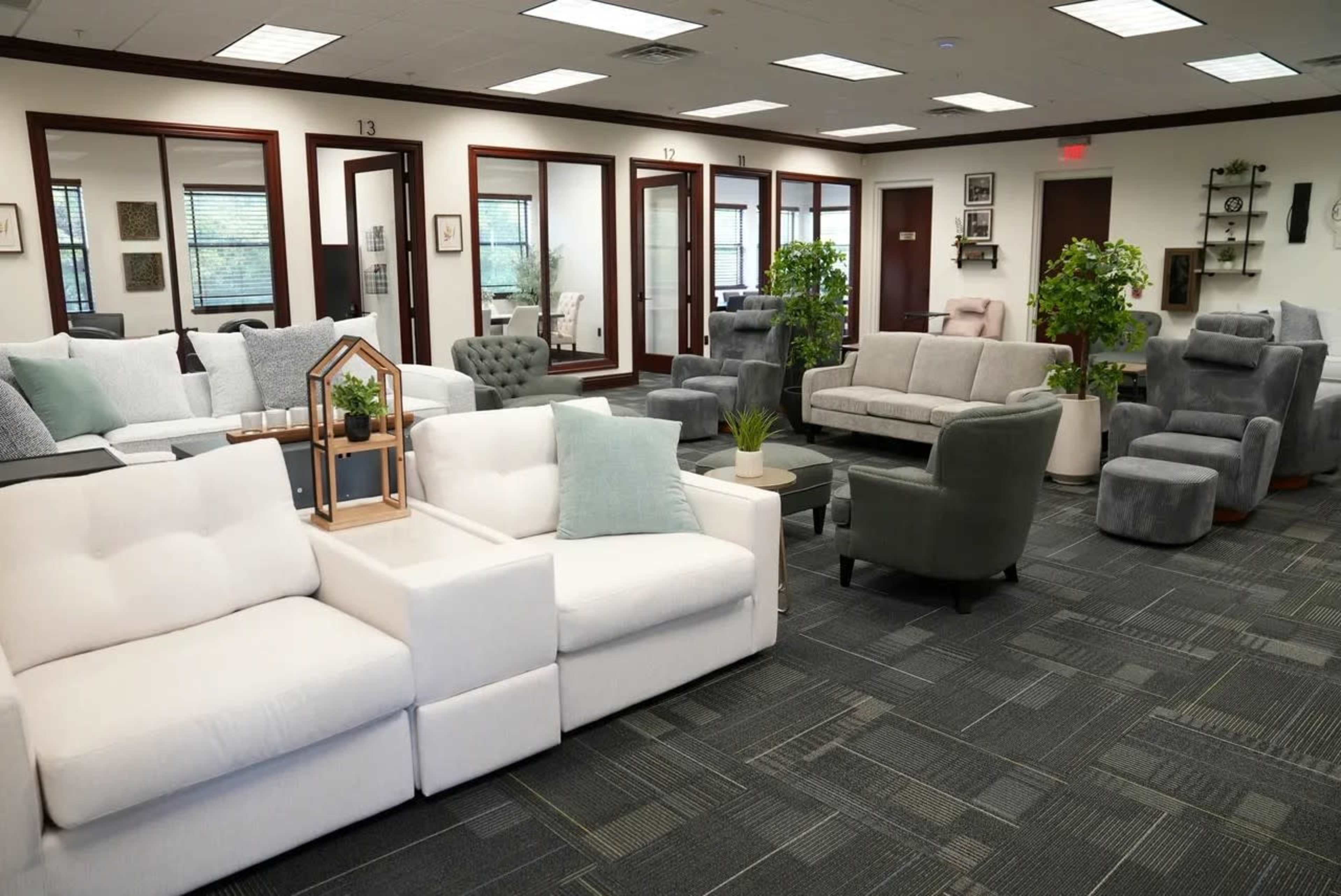 The image shows a spacious furniture showroom featuring various seating arrangements, including sofas, recliners, and decorative plants in an indoor setting.