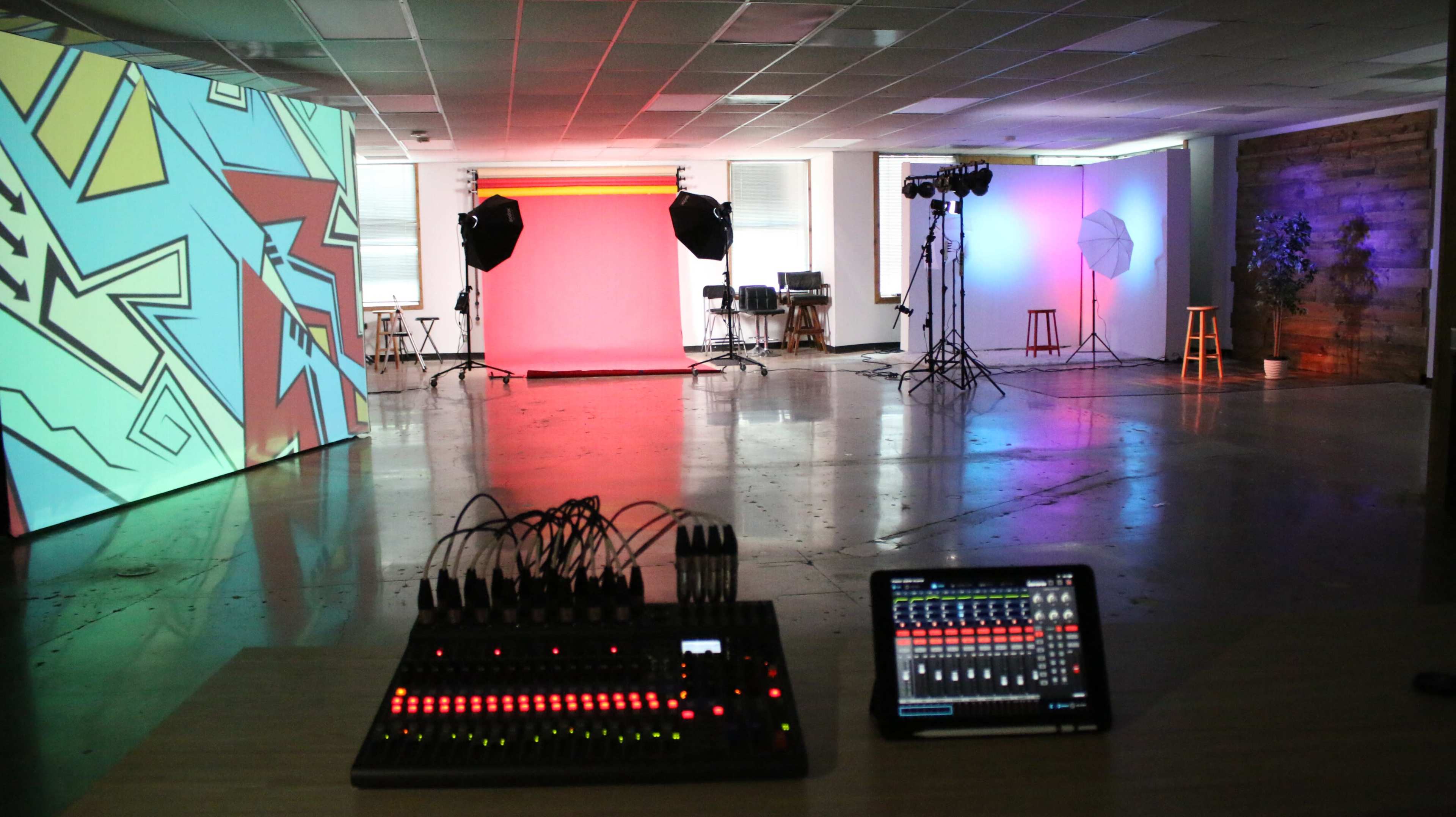 A spacious studio with colorful projected backgrounds, lighting equipment, and a sound mixing console on a table in the foreground.