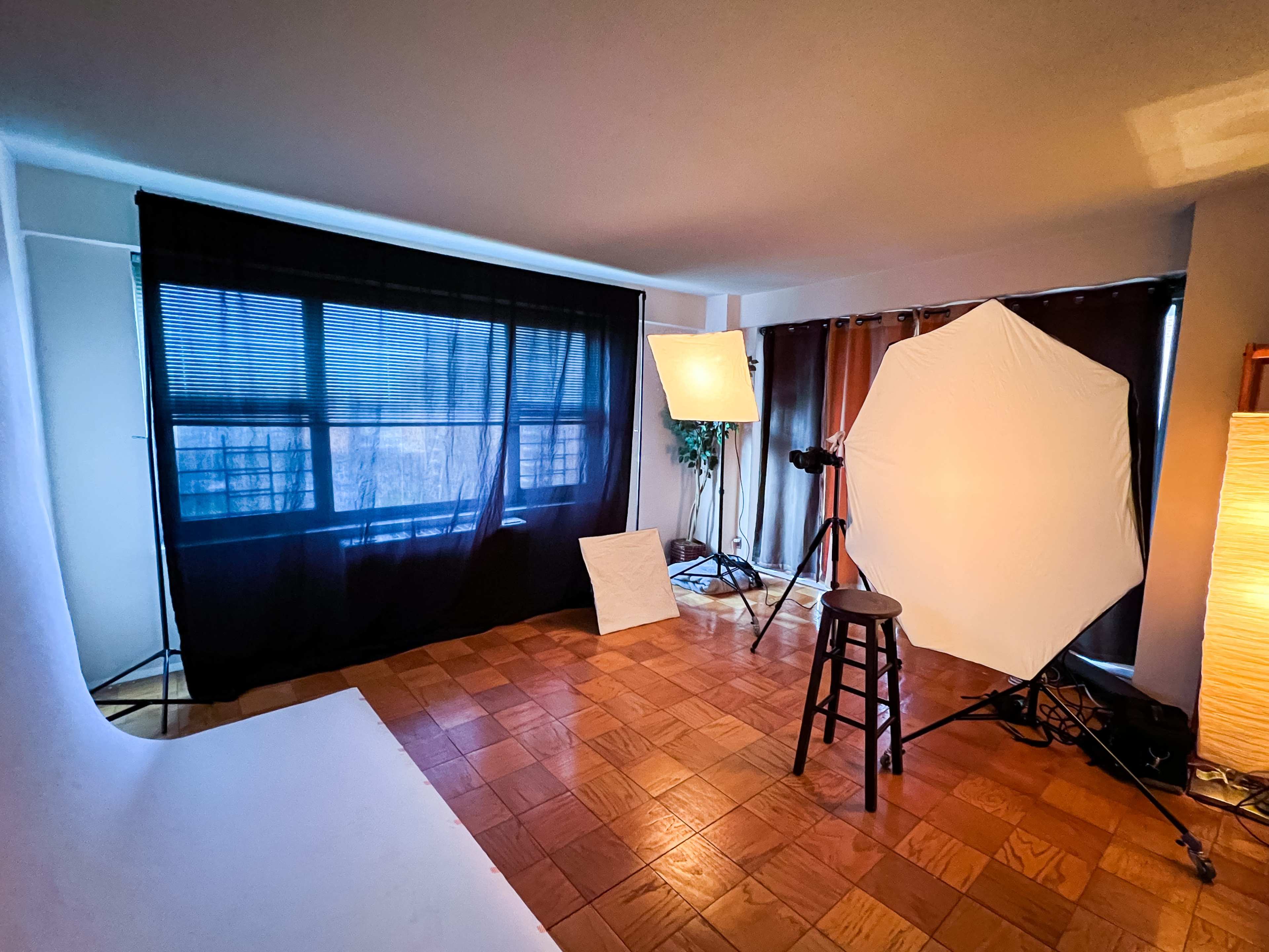 A photography studio setup with lighting equipment, backdrops, and a stool positioned on a wooden floor.