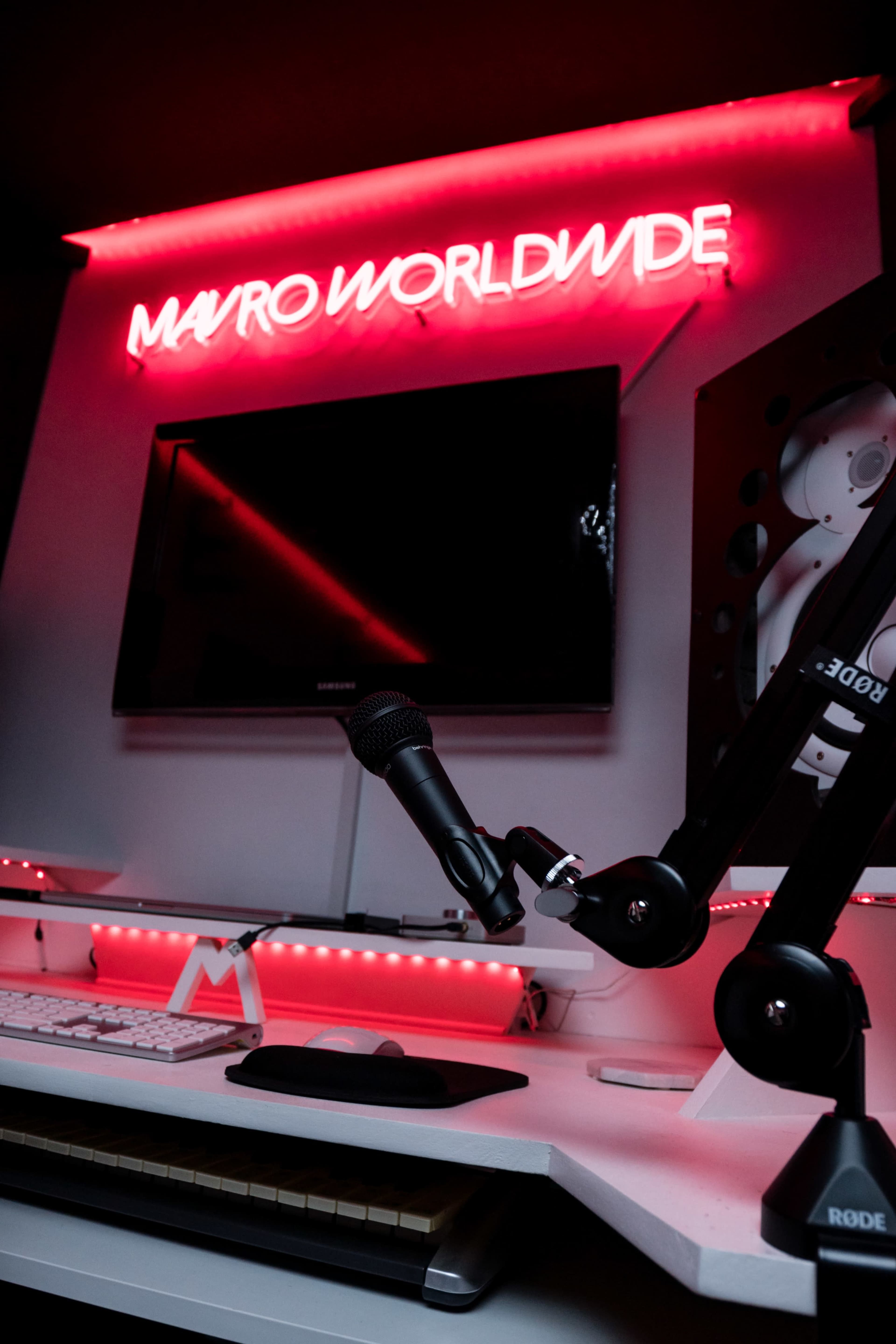 A modern workspace features a neon sign reading "MAVRO WORLDWIDE," a microphone, and sleek electronic equipment.