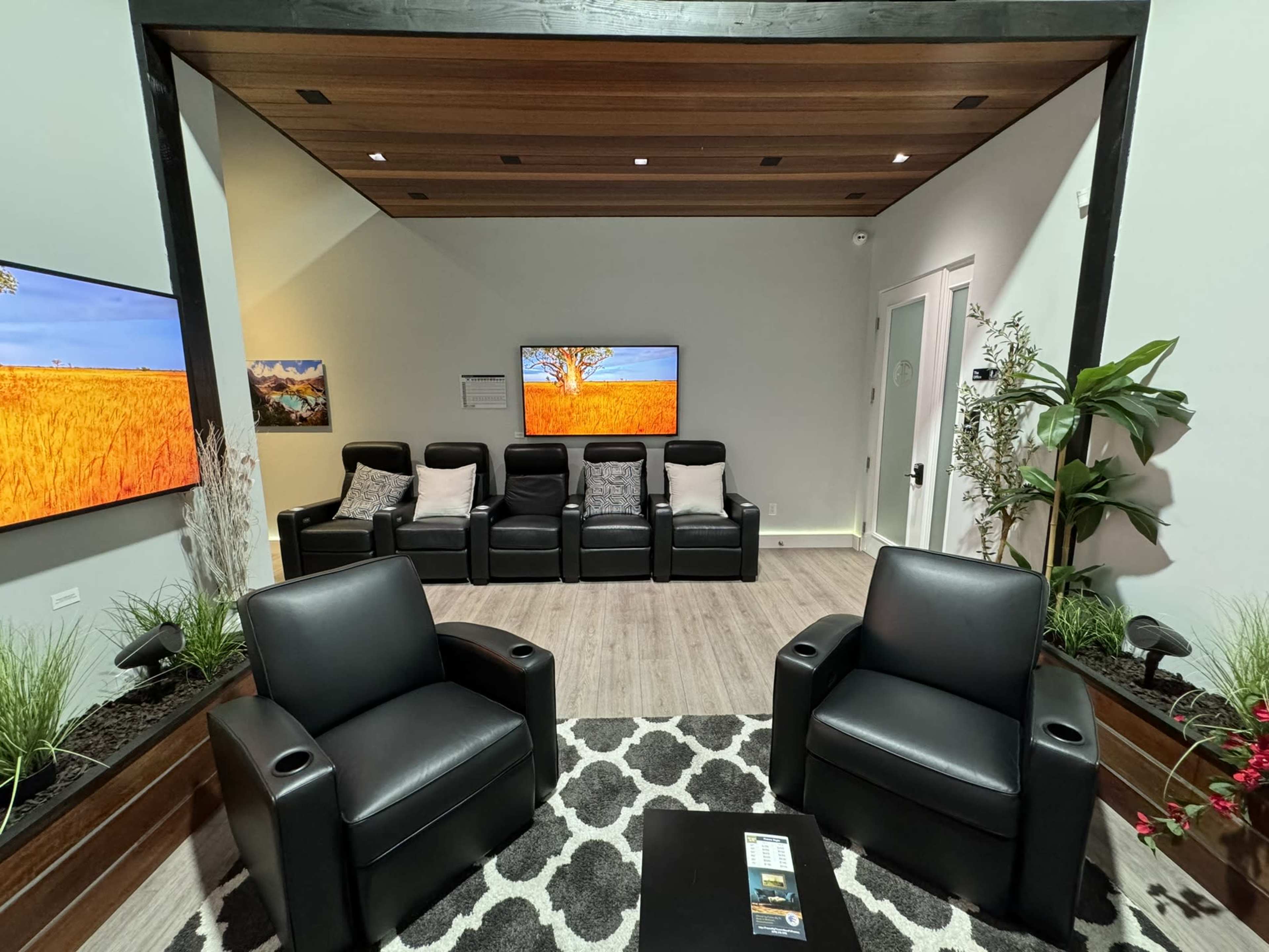 A modern room featuring black leather seating, a patterned rug, and two wall-mounted screens displaying artwork.