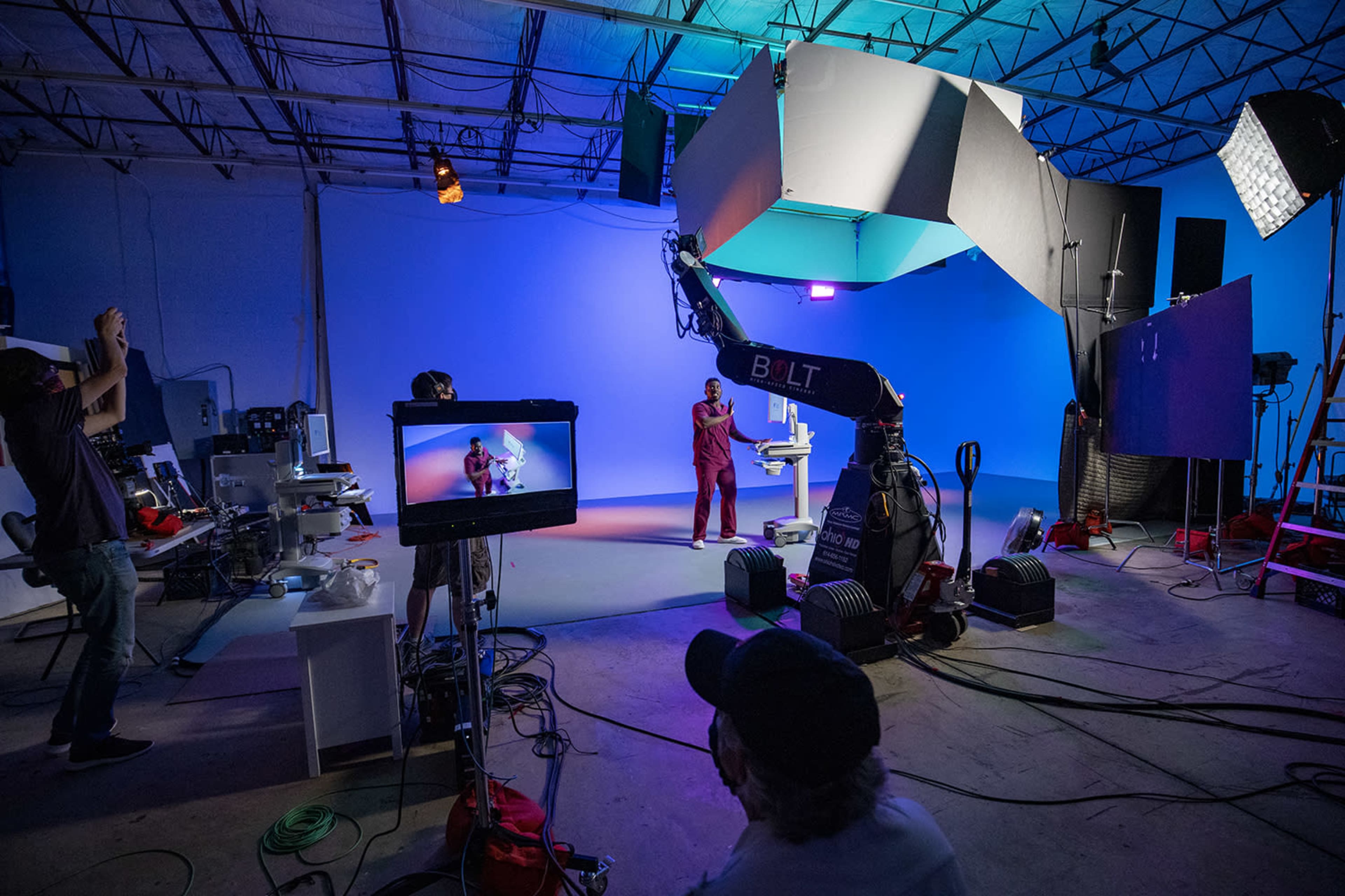 A film production crew sets up equipment in a studio with blue lighting for a video shoot.