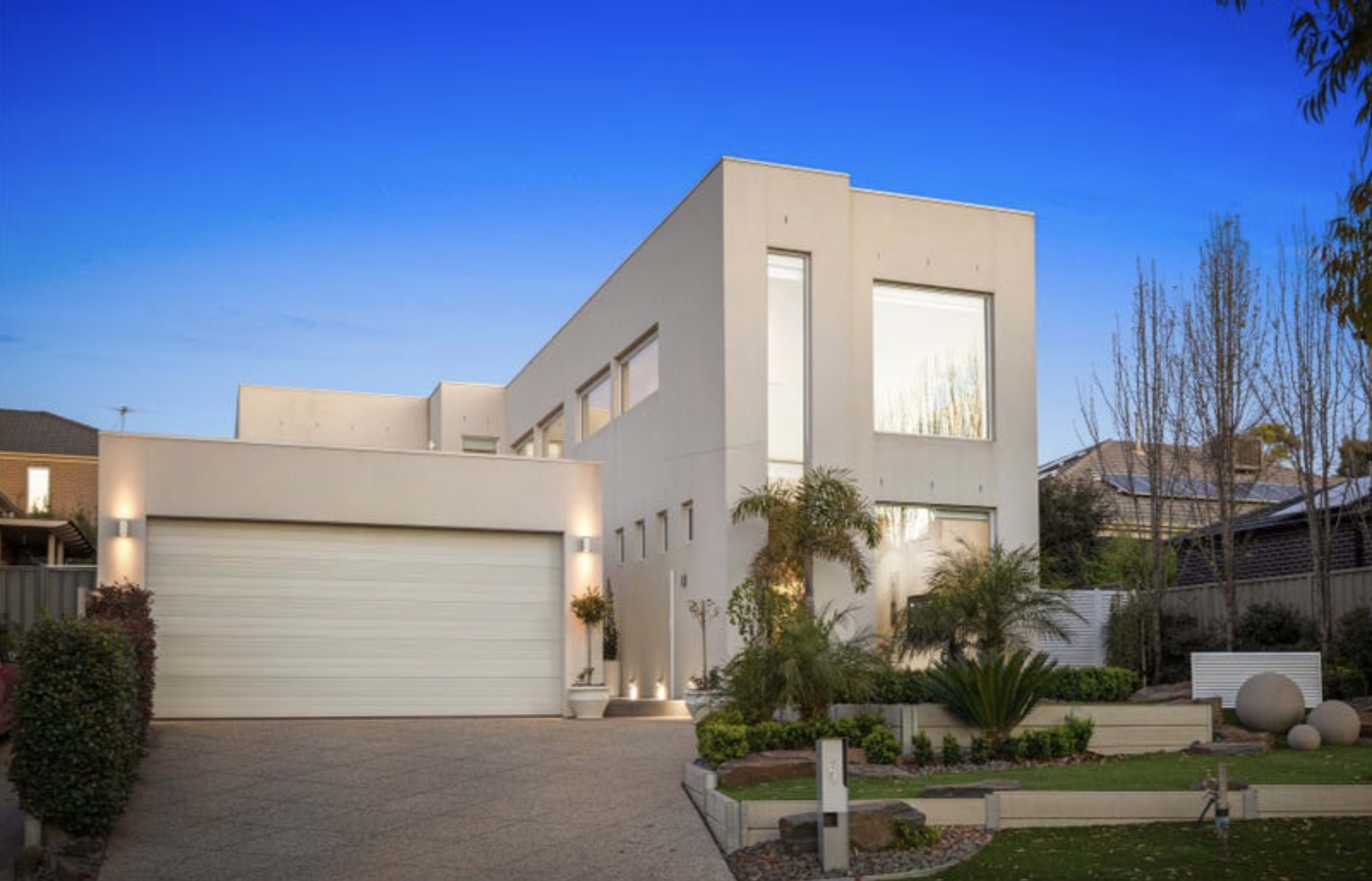 A modern two-story house with large windows and a landscaped front yard.