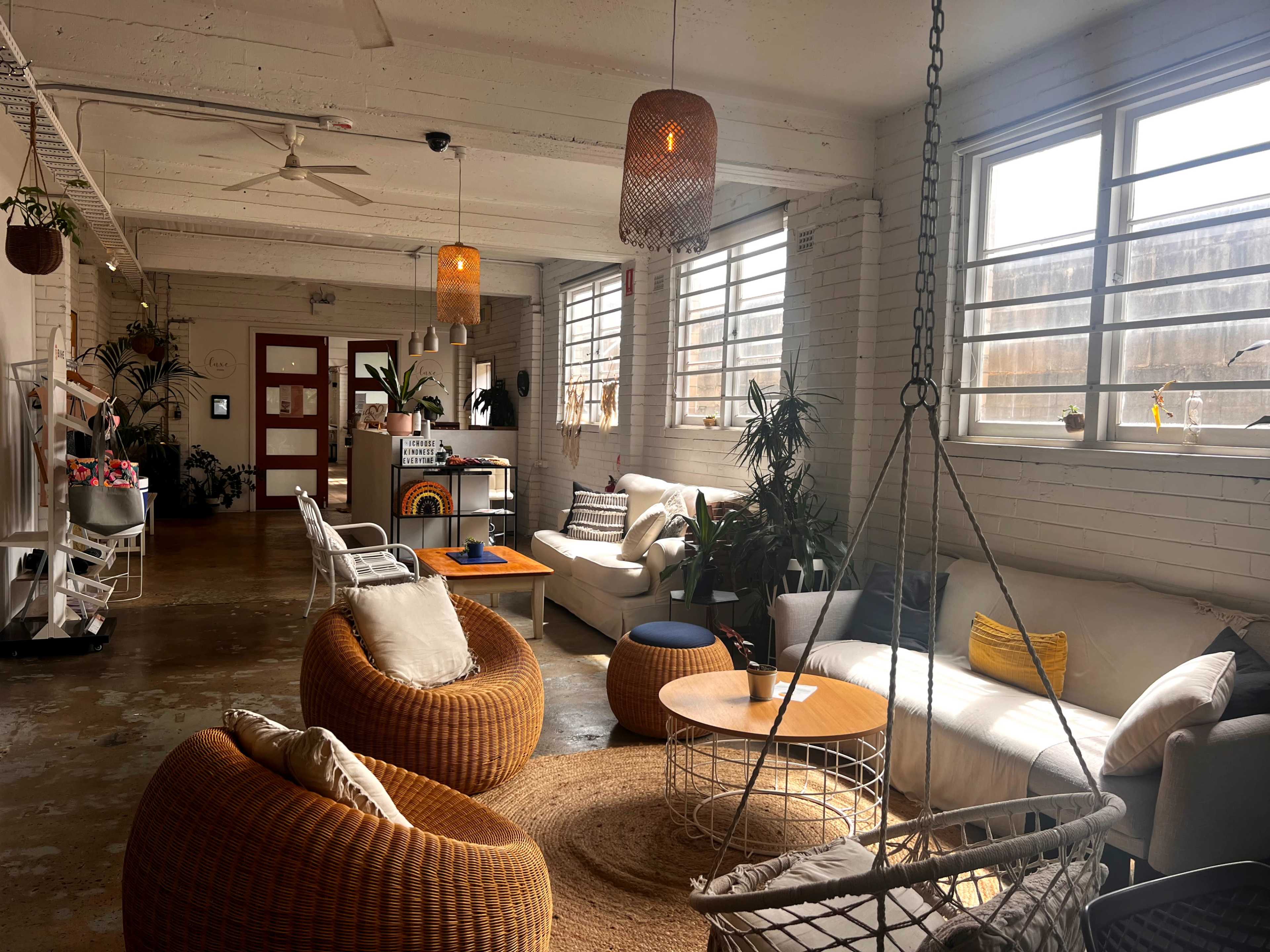 The image showcases a spacious, well-lit lounge area featuring a variety of seating options, including woven chairs and sofas, along with potted plants and large windows.