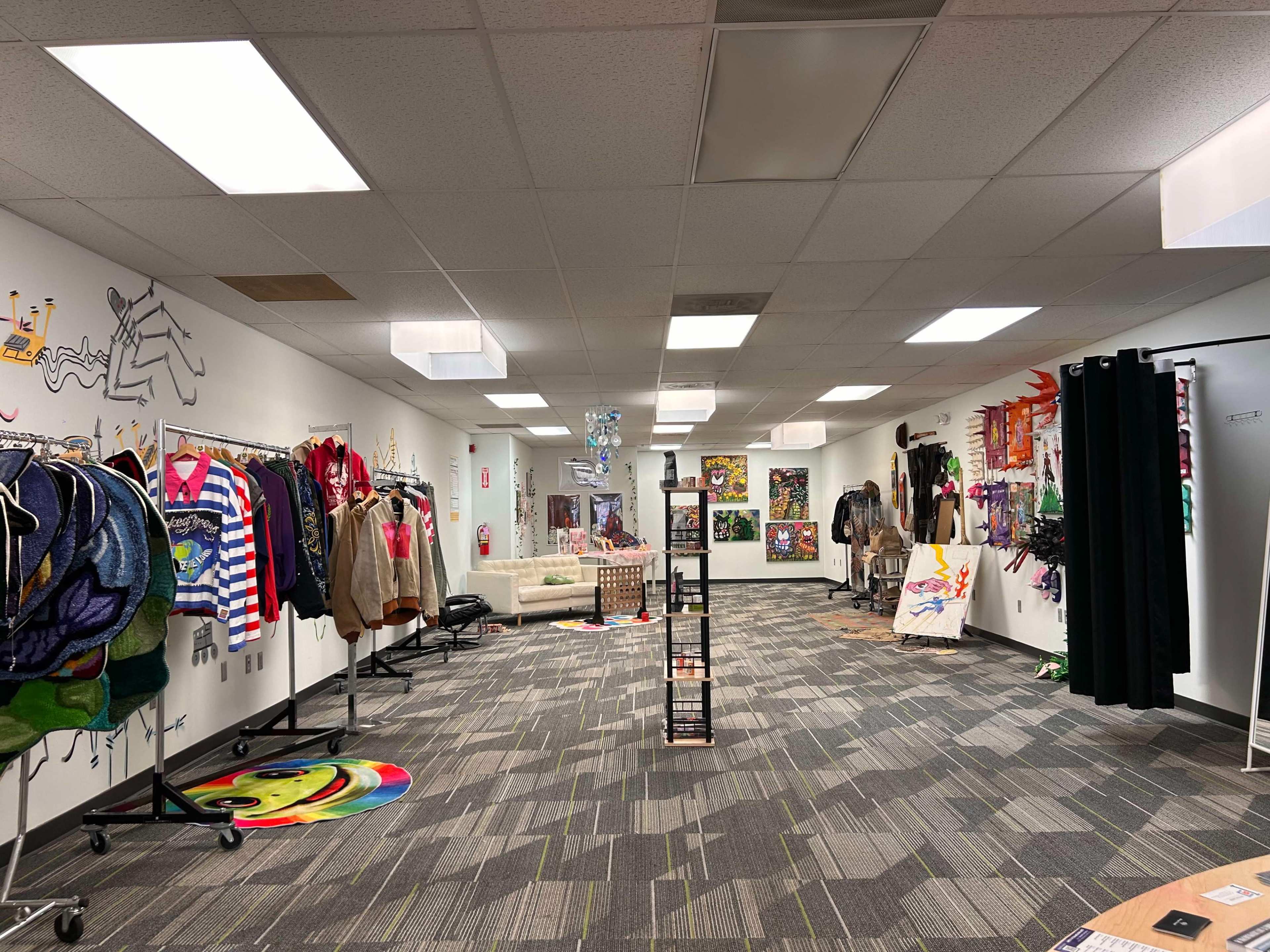 The spacious room features clothing racks with various garments, colorful artwork on the walls, and a seating area towards the back.