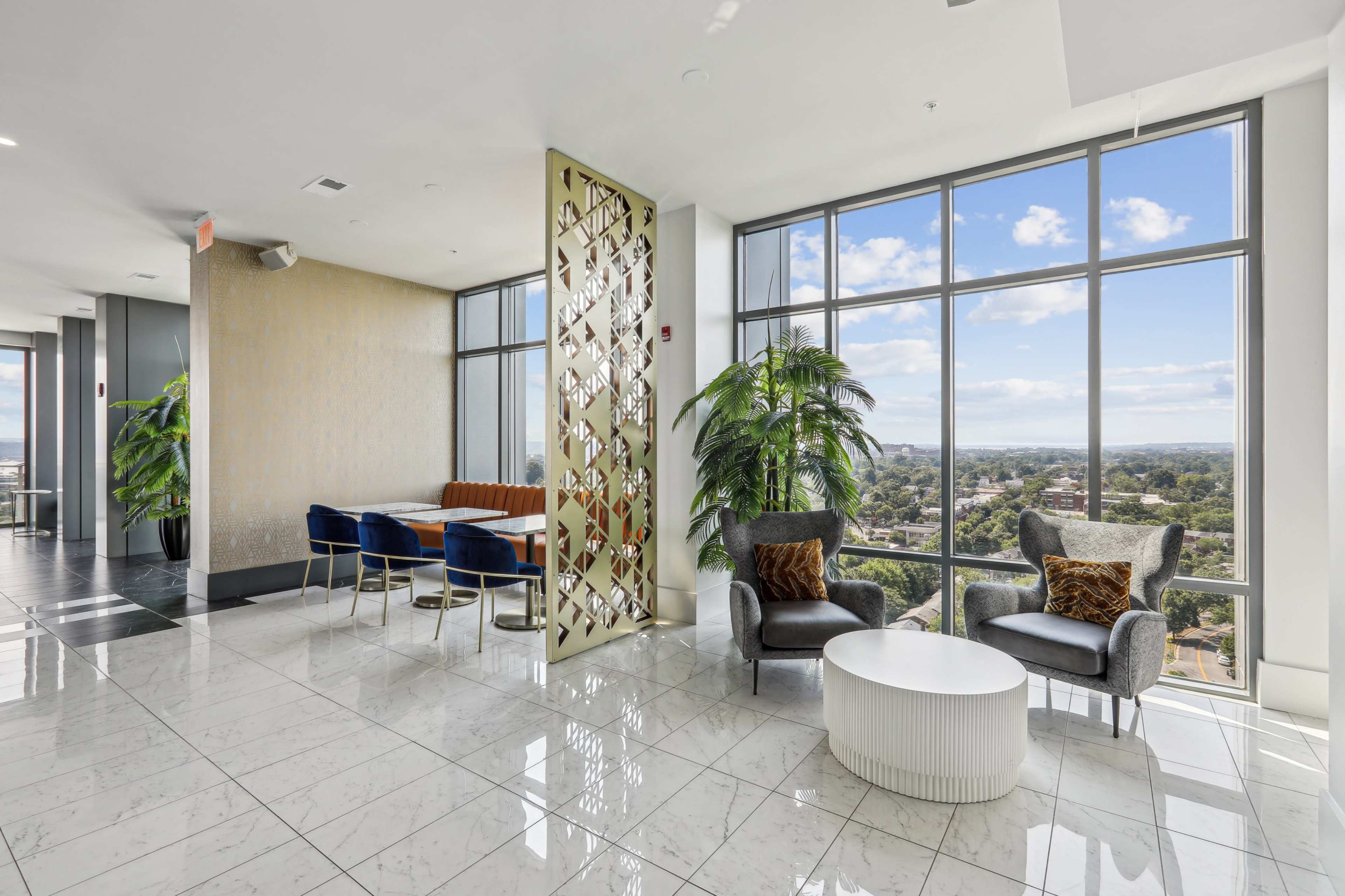 A modern lounge area with large windows, a decorative partition, and plush seating arrangements beside potted plants.
