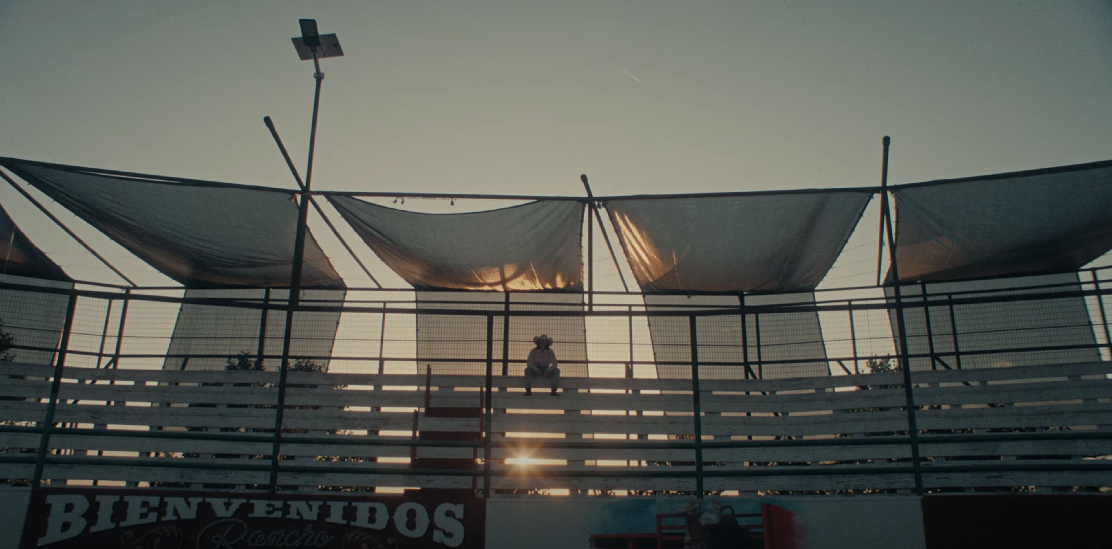 A person sits alone in the bleachers of a sports arena with a sunset illuminating the scene.