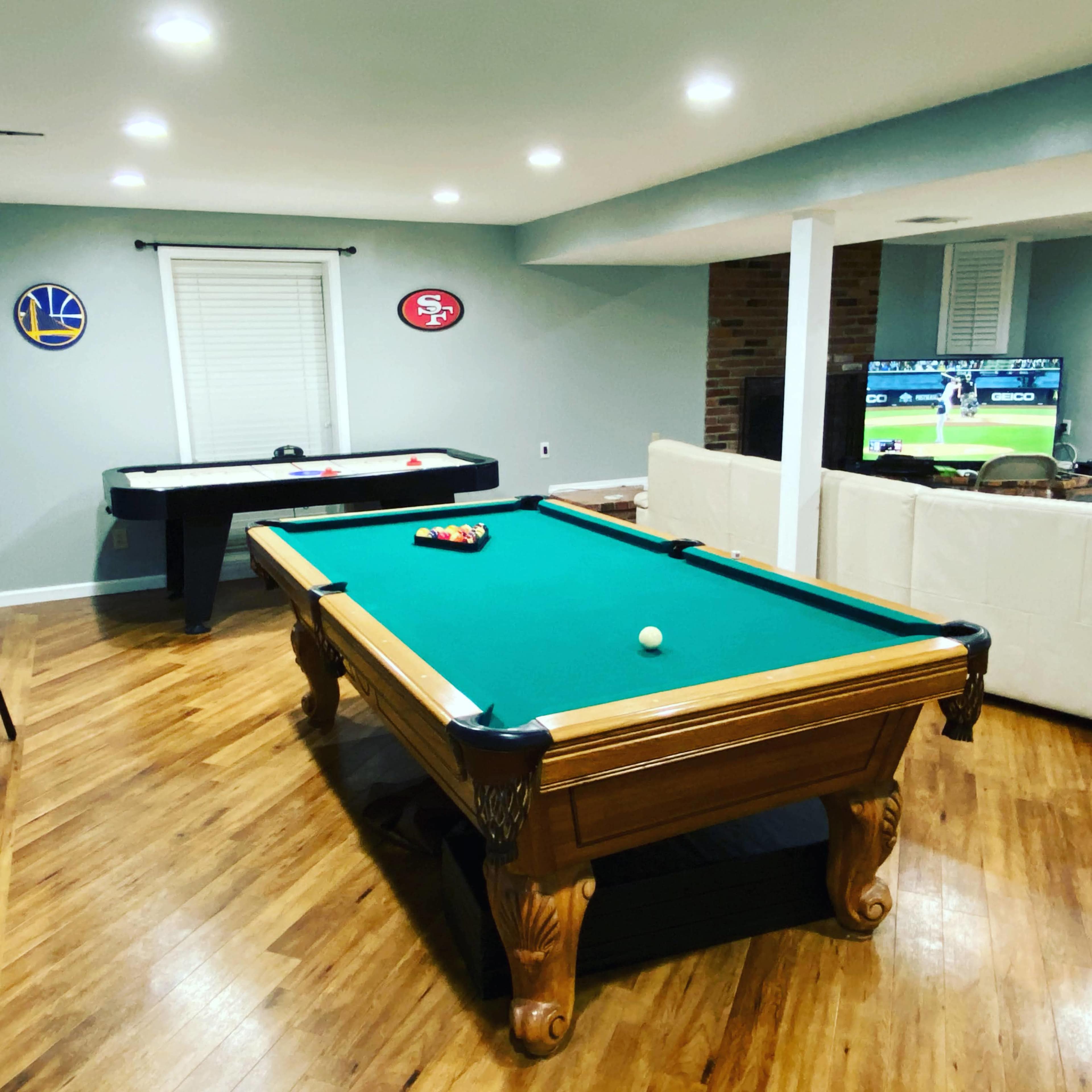 A recreation room featuring a pool table, an air hockey table, and a television displaying a sports game.